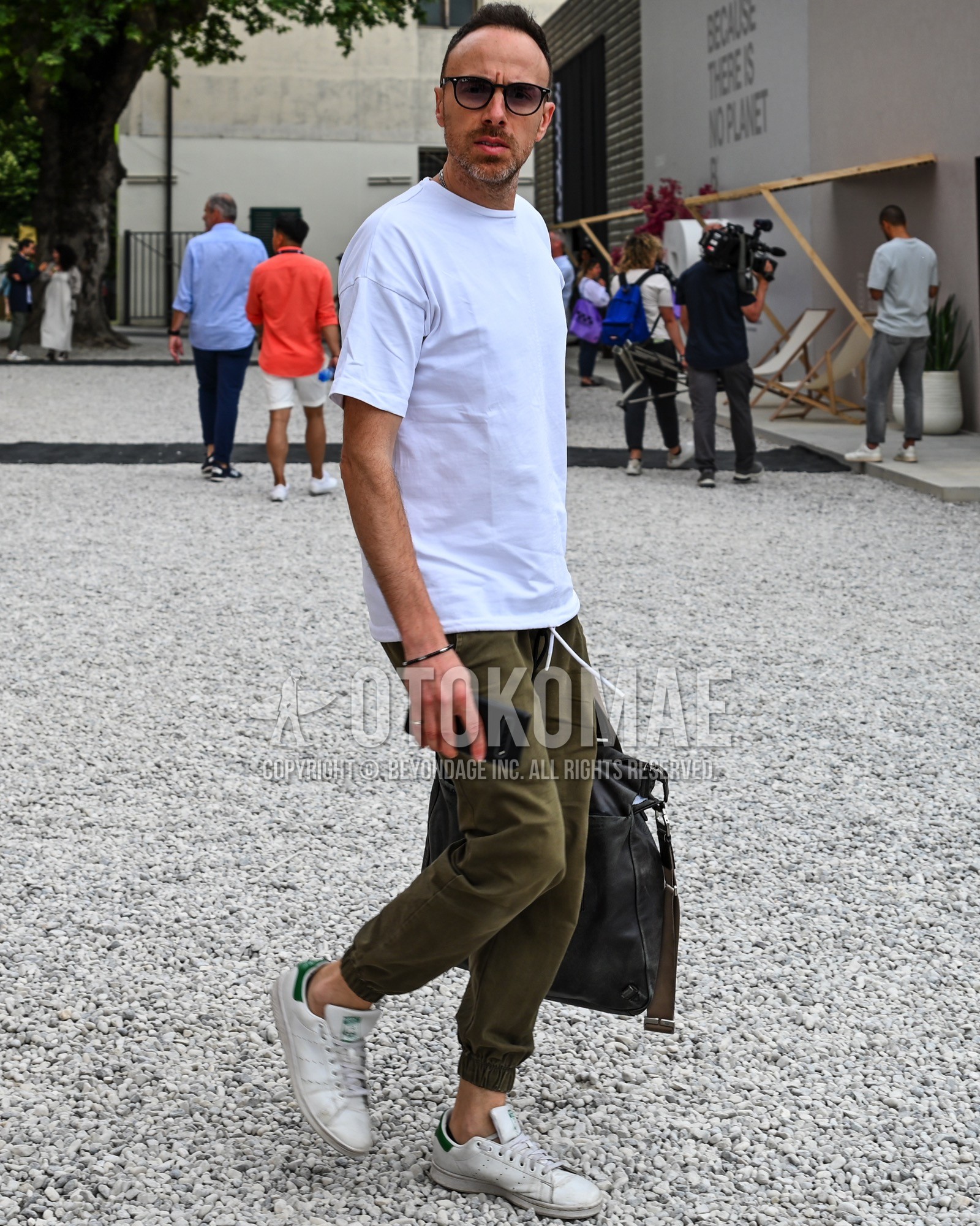 Men's spring summer outfit with brown plain sunglasses, white plain t-shirt, olive green plain jogger pants/ribbed pants, black plain tote bag.
