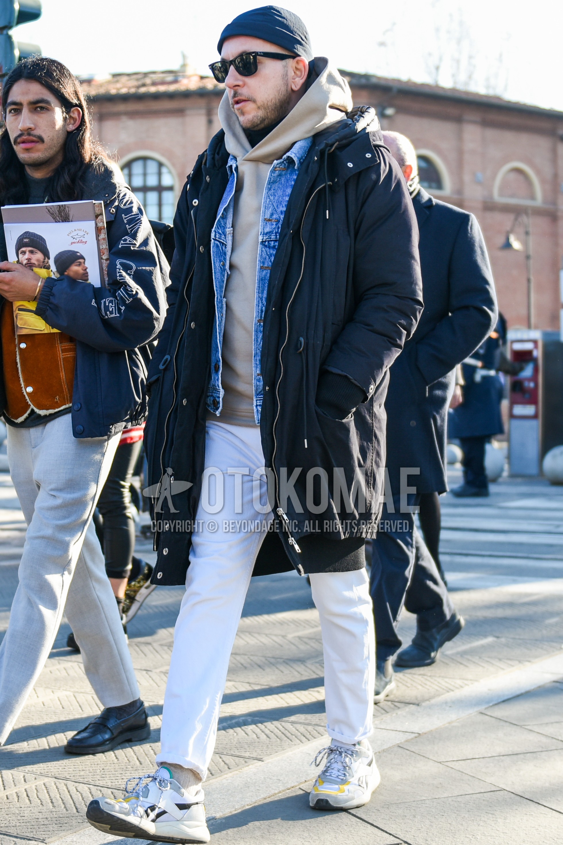 Men's autumn winter outfit with dark gray plain knit cap, black plain sunglasses, black plain hooded coat, blue plain denim jacket, beige plain hoodie, white plain cotton pants, beige plain socks, white low-cut sneakers.