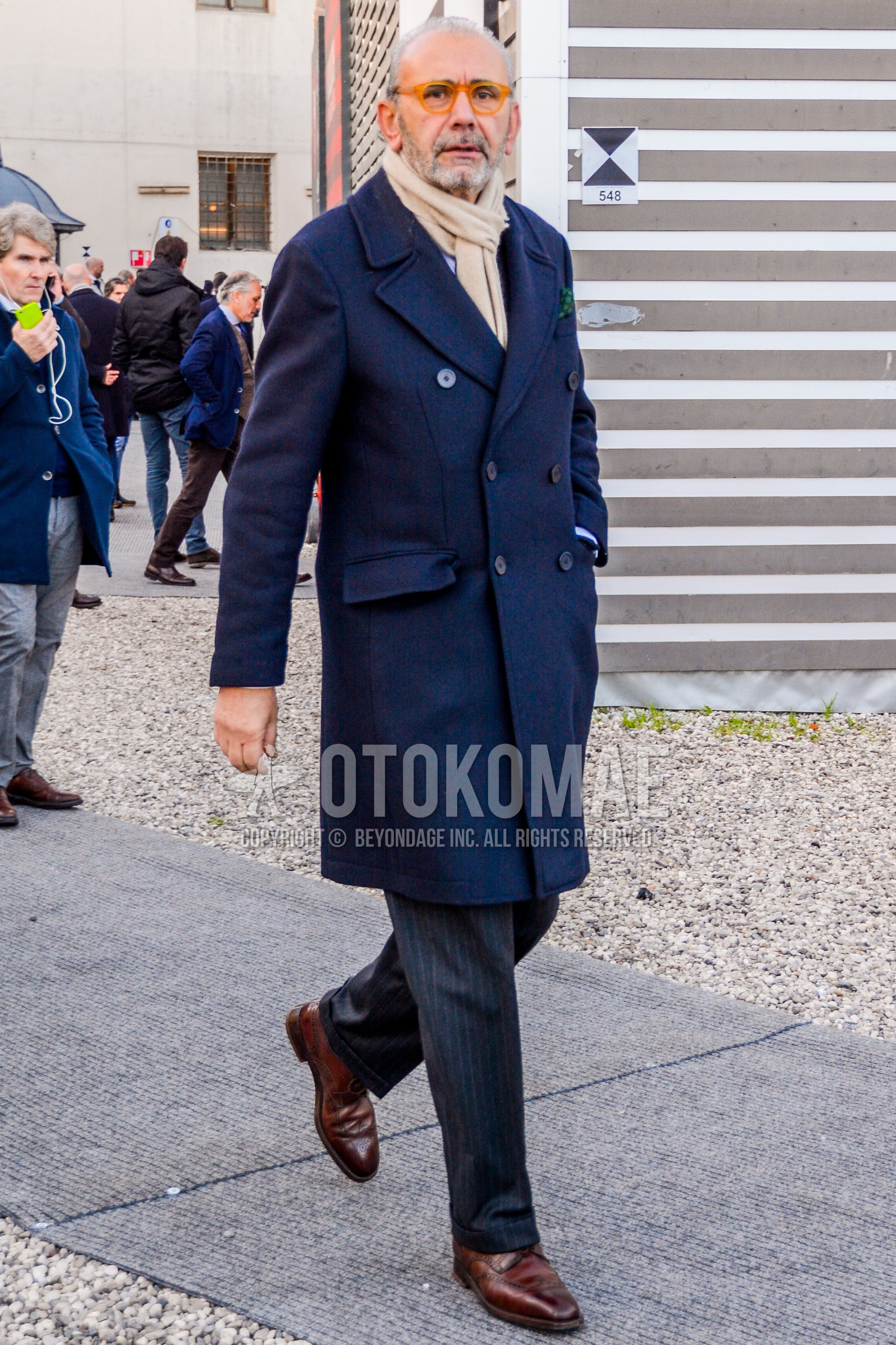 Men's winter outfit with plain glasses, beige plain scarf, navy plain chester coat, dark gray stripes slacks, brown wing-tip shoes leather shoes.