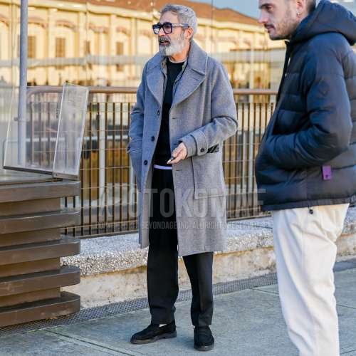 黒無地のメガネ、グレー無地のアルスターコート、グレー無地のインナーダウン、黒無地のトレーナー、白無地のTシャツ、ダークグレー無地のスラックス、白無地のソックス、黒コインローファーの革靴、黒スエードシューズの革靴を合わせた秋冬のメンズコーデ・着こなし。