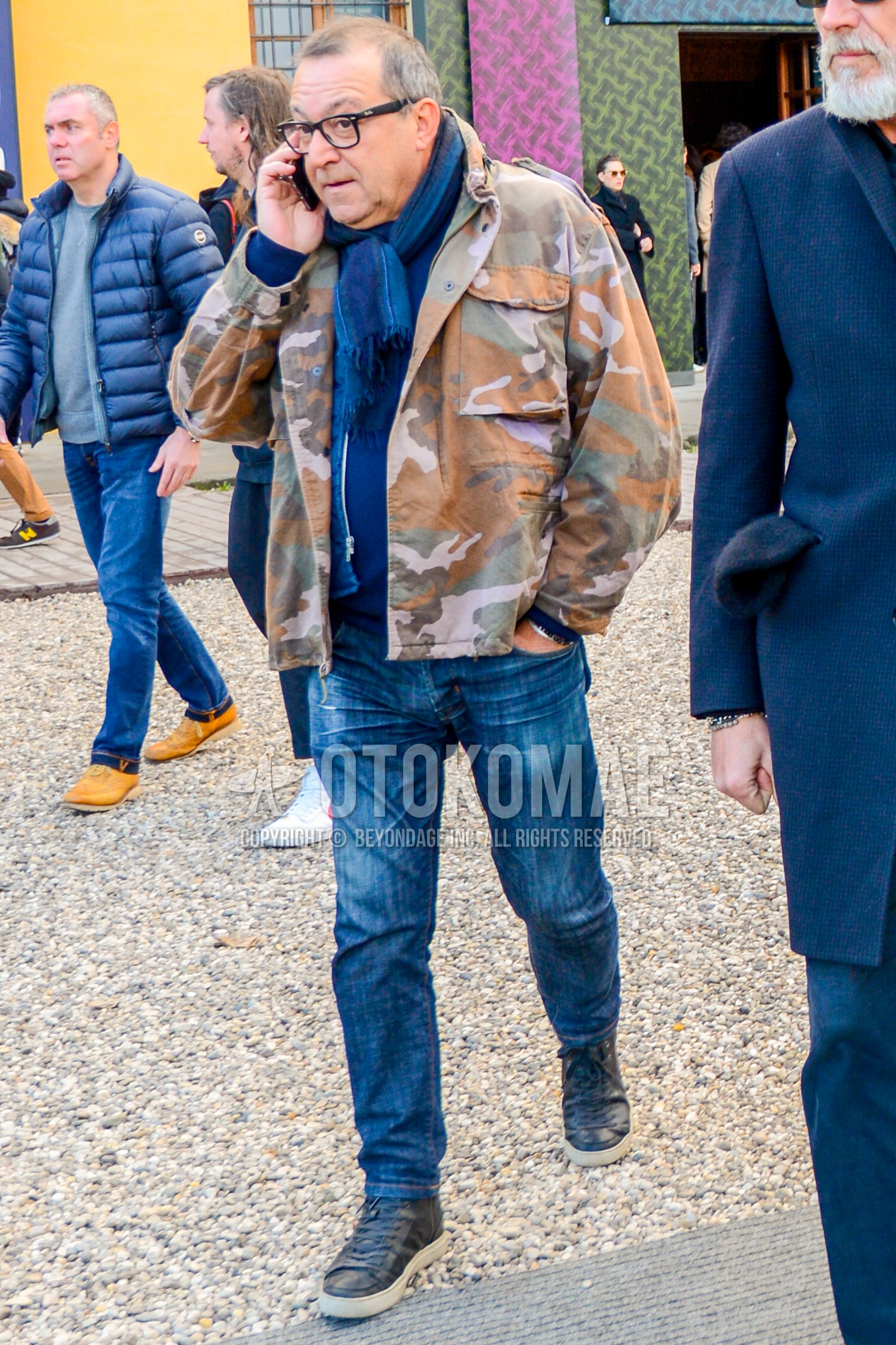 Men's winter outfit with plain glasses, navy plain scarf, multi-color camouflage M-65, blue plain denim/jeans, black leather shoes.