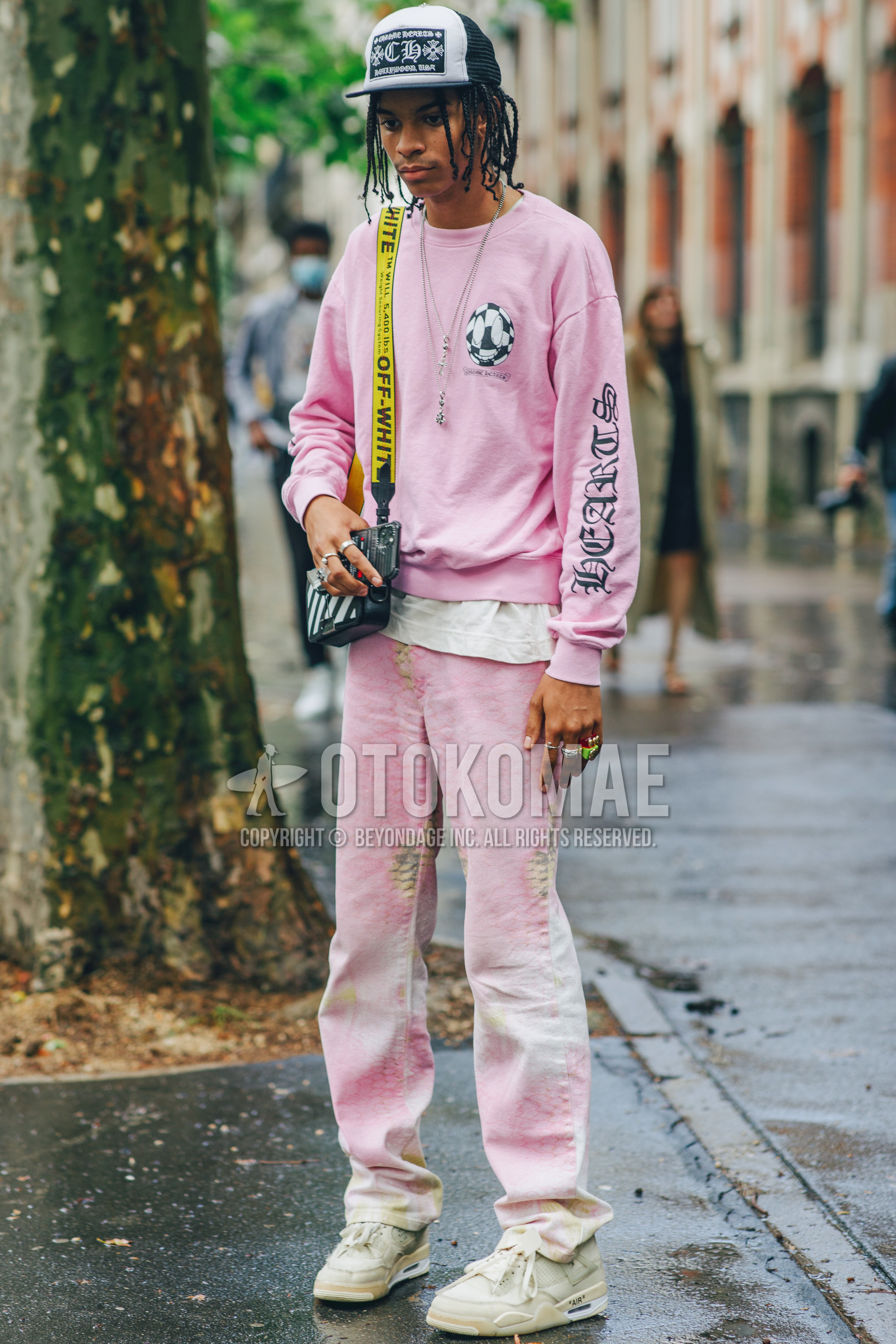 Men's spring summer outfit with black graphic baseball cap, pink plain sweatshirt, pink plain sweatpants, white high-cut sneakers, black bag shoulder bag, pink suit casual setup.