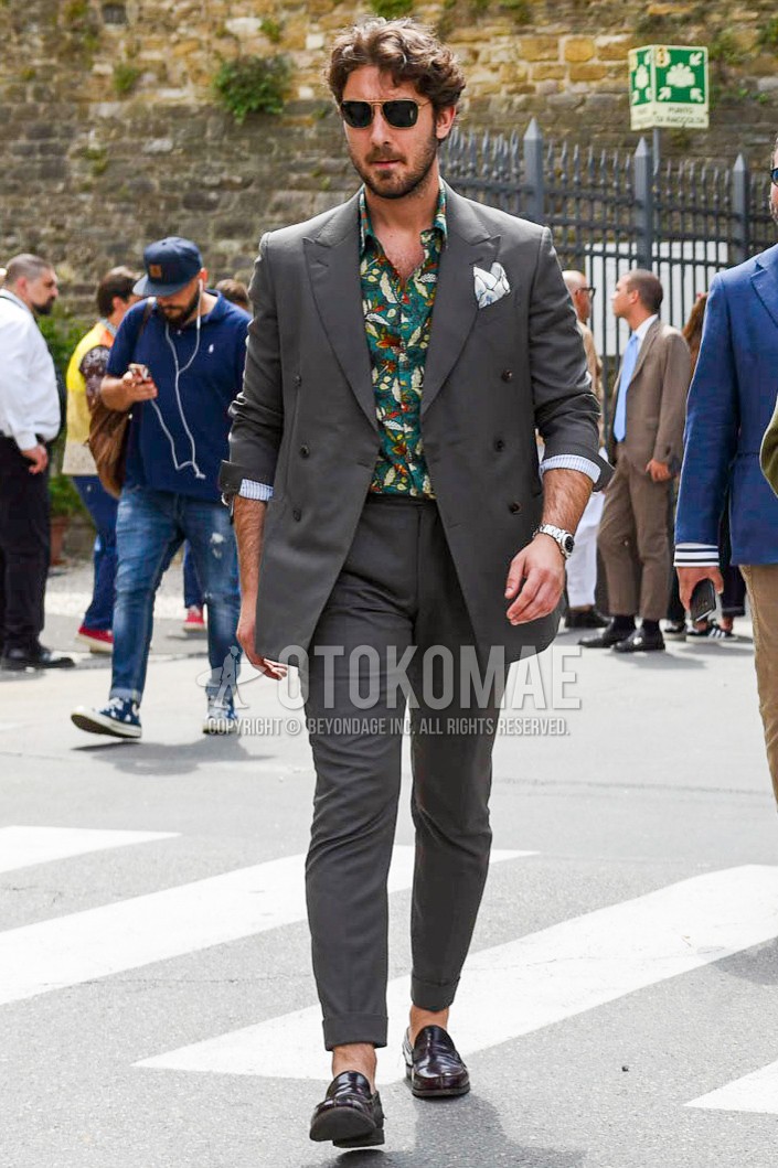 Men's spring summer autumn outfit with black plain sunglasses, green botanical shirt, brown coin loafers leather shoes, dark gray plain suit.