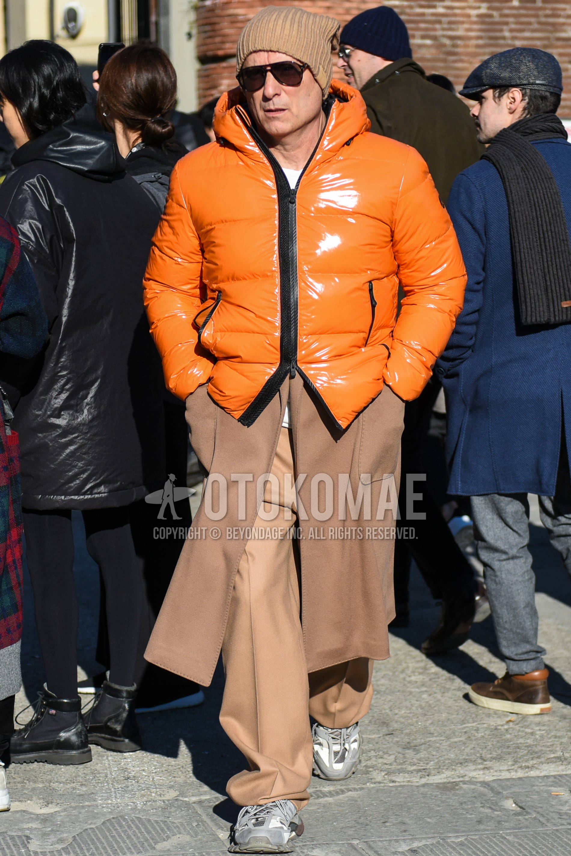 Men's winter outfit with beige plain knit cap, black plain sunglasses, orange plain down jacket, beige plain chester coat, beige plain chinos, gray low-cut sneakers.