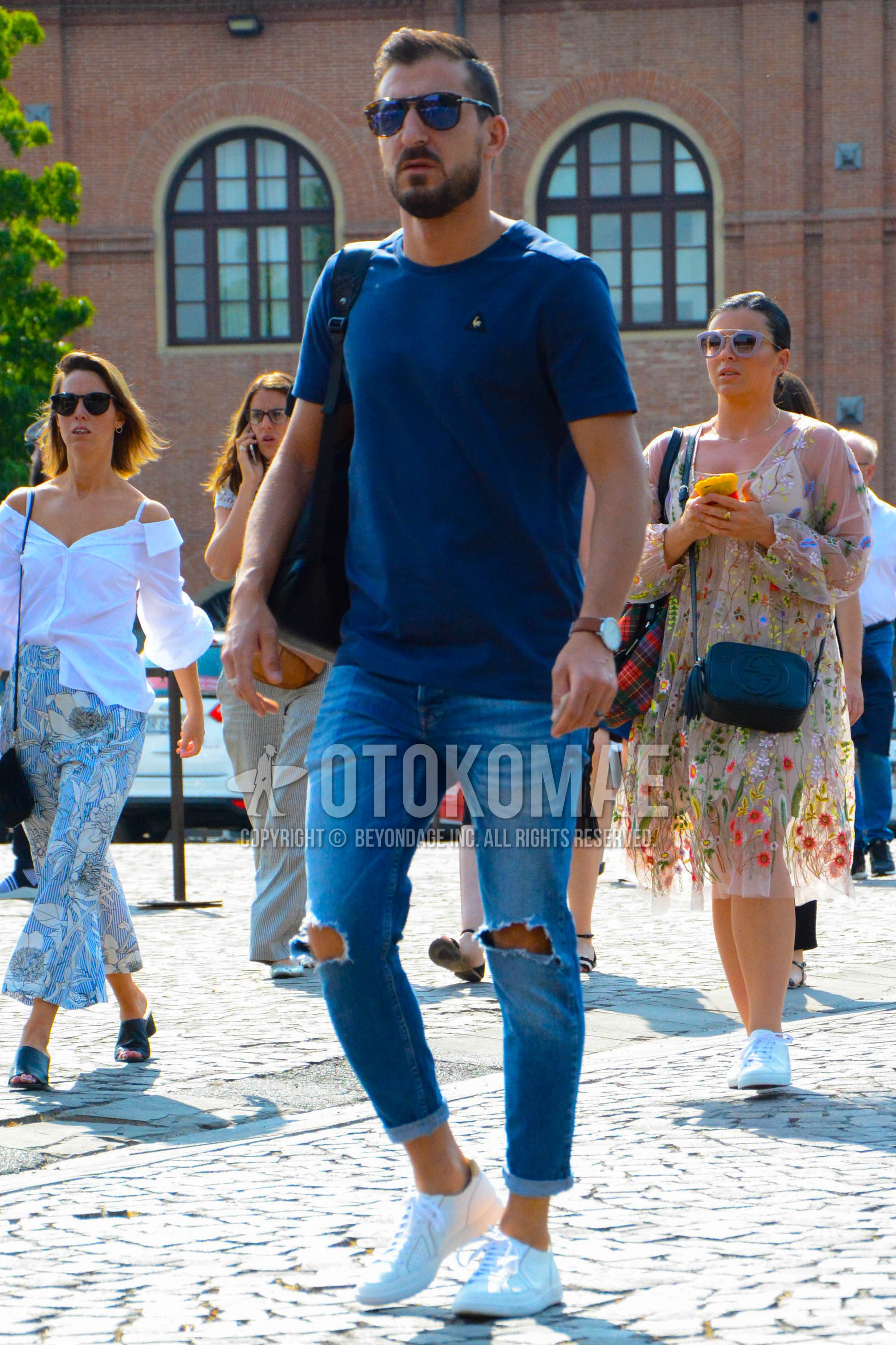 Men's spring summer outfit with brown tortoiseshell sunglasses, navy one point t-shirt, blue plain damaged jeans, white low-cut sneakers, black plain shoulder bag.