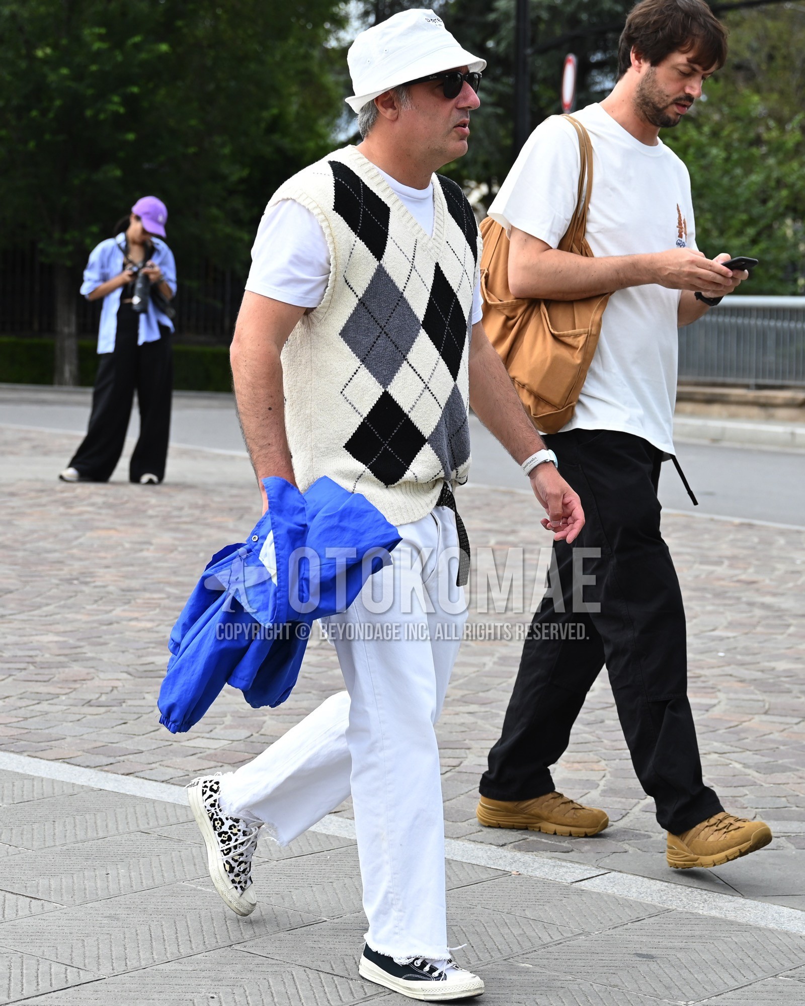 Men's spring summer outfit with white one point bucket hat, white whole pattern casual vest, white plain t-shirt, white plain denim/jeans, black low-cut sneakers.