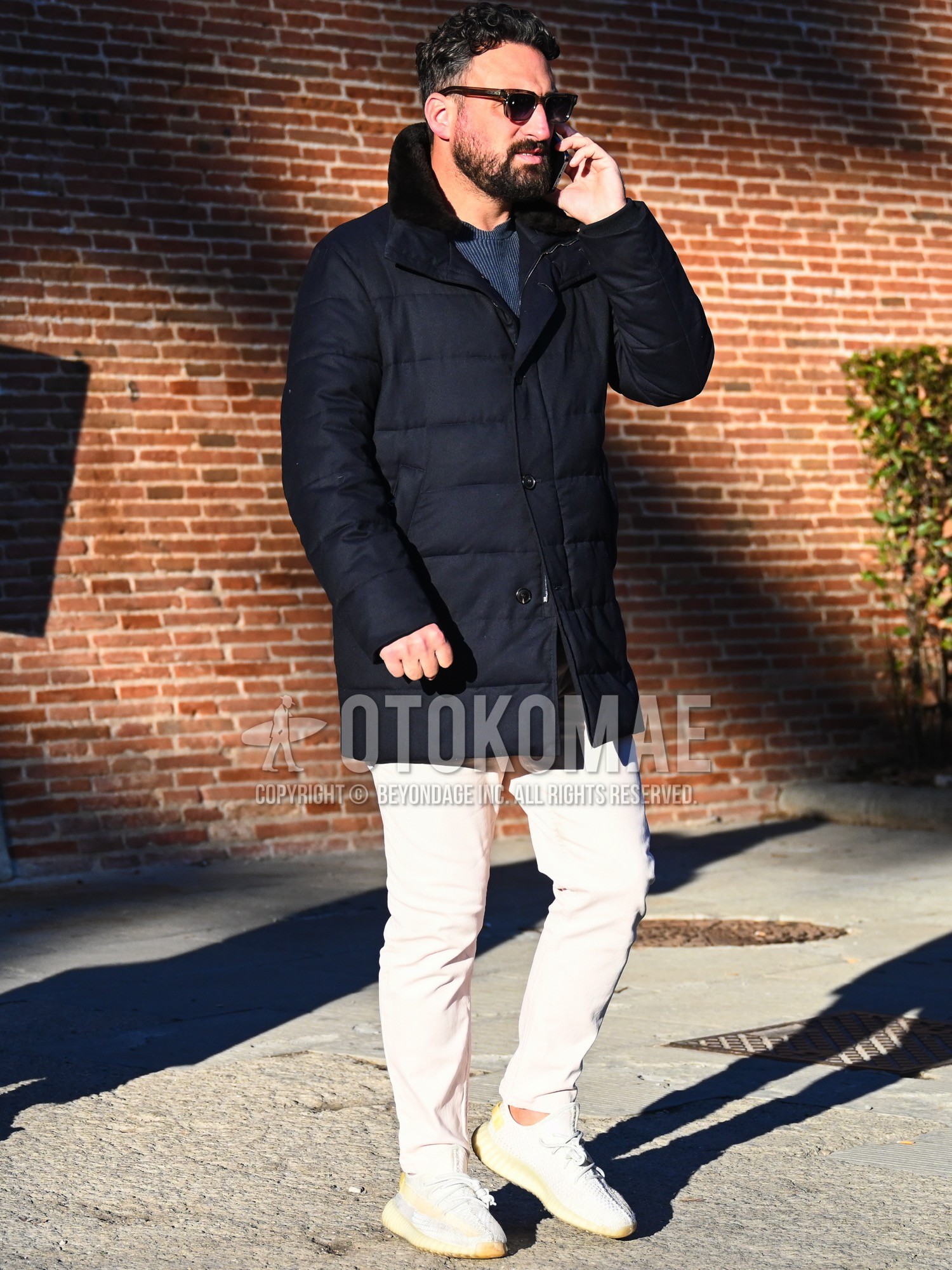 Men's autumn winter outfit with brown tortoiseshell sunglasses, navy plain down jacket, blue plain sweater, white plain chinos, white low-cut sneakers.