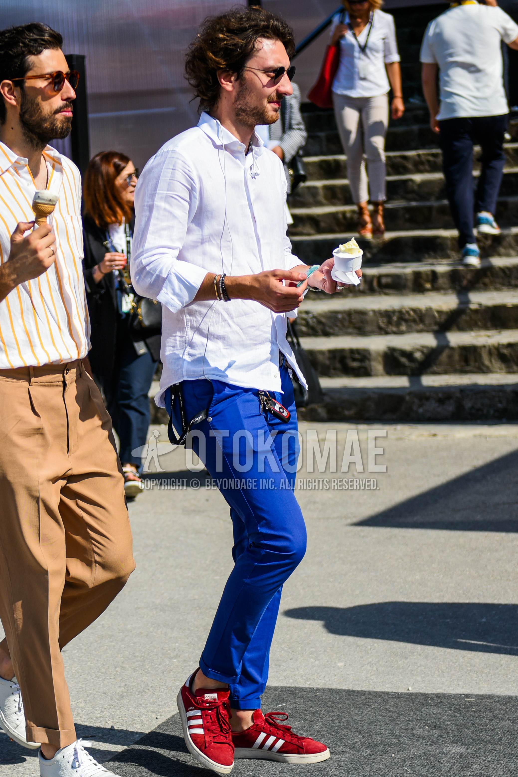 Men's spring summer outfit with black plain sunglasses, white plain shirt, blue plain chinos, red low-cut sneakers.