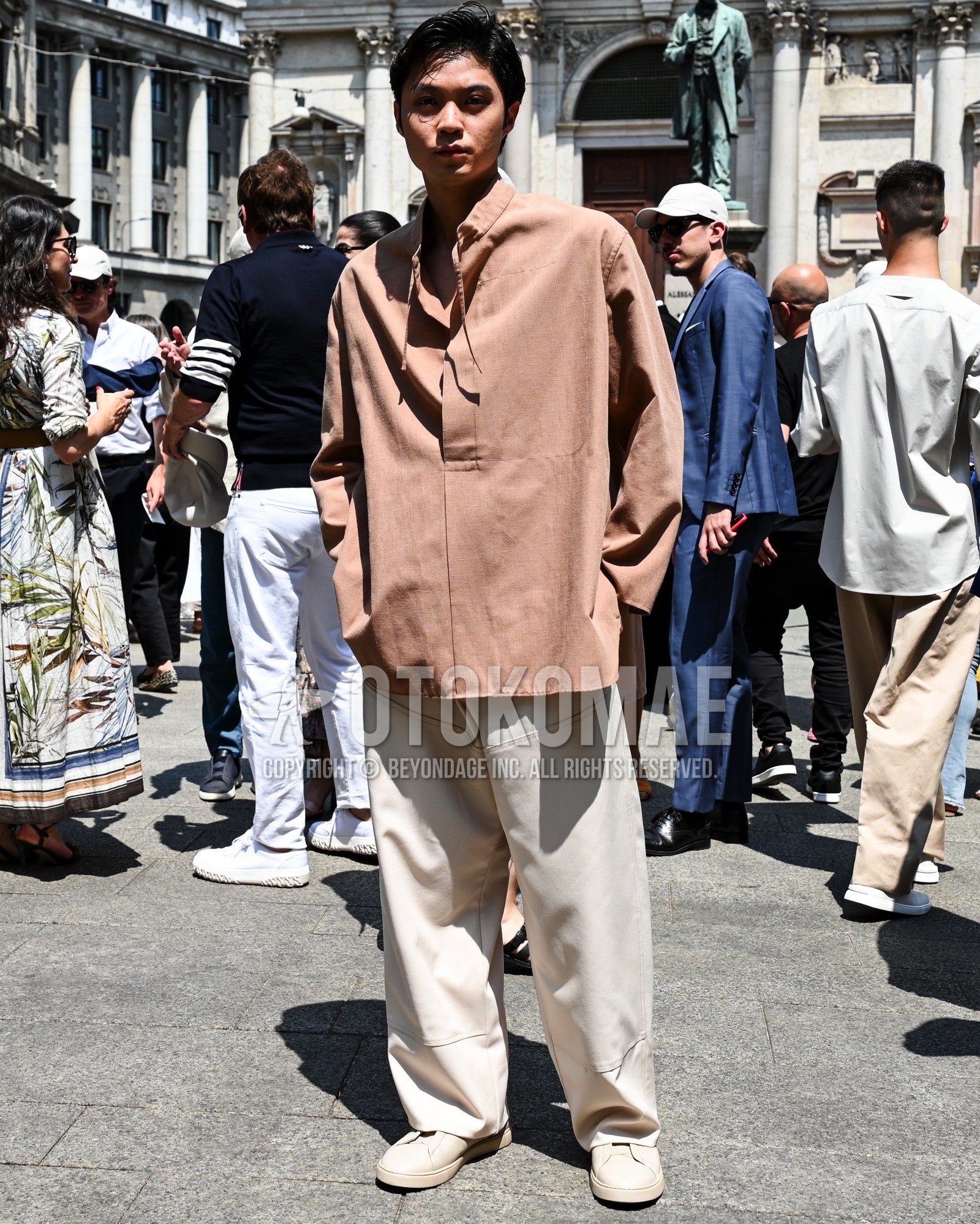 Men's spring summer autumn outfit with beige plain shirt, white plain wide pants, white low-cut sneakers.