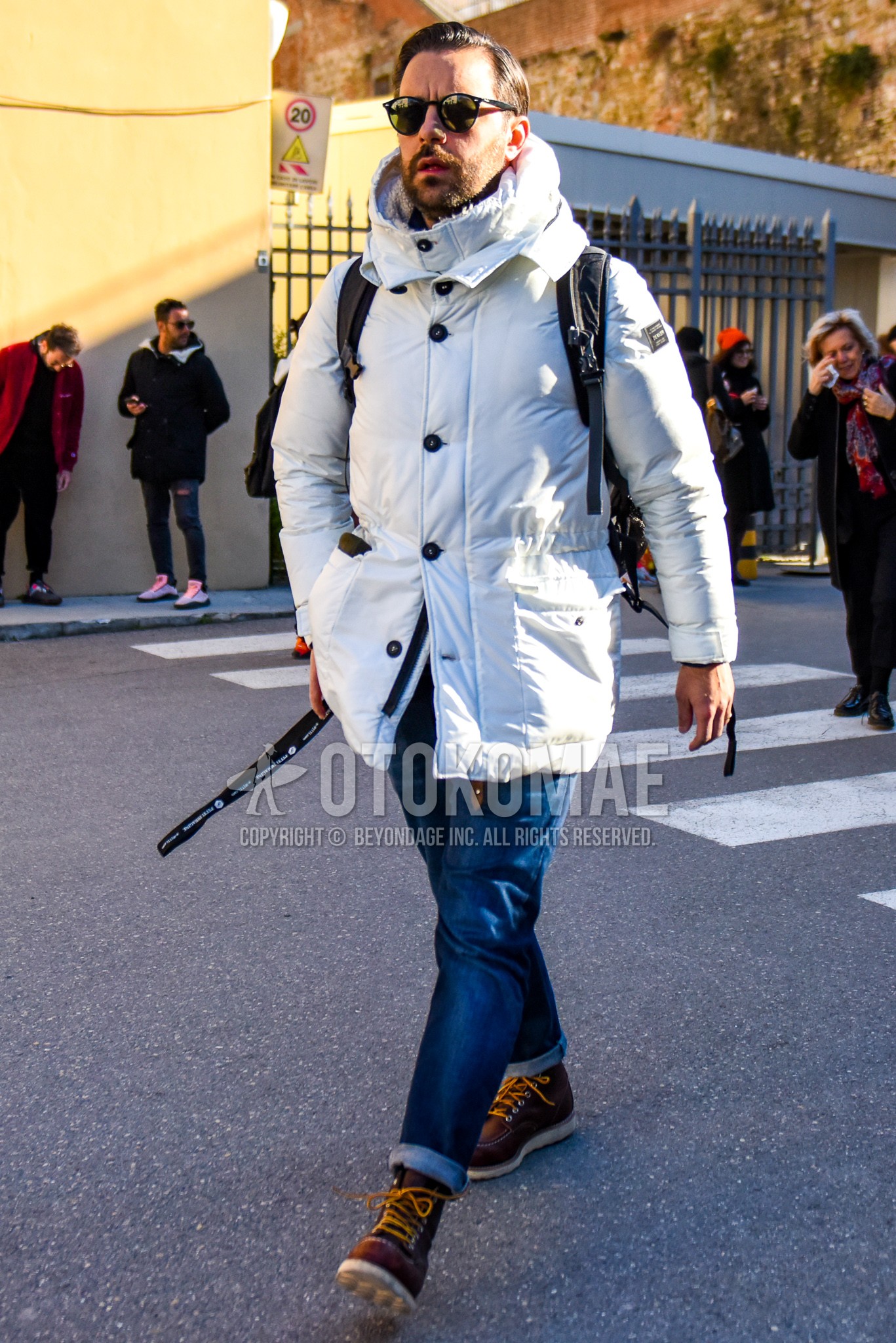 Men's winter outfit with black plain sunglasses, white plain down jacket, blue plain denim/jeans, brown work boots.