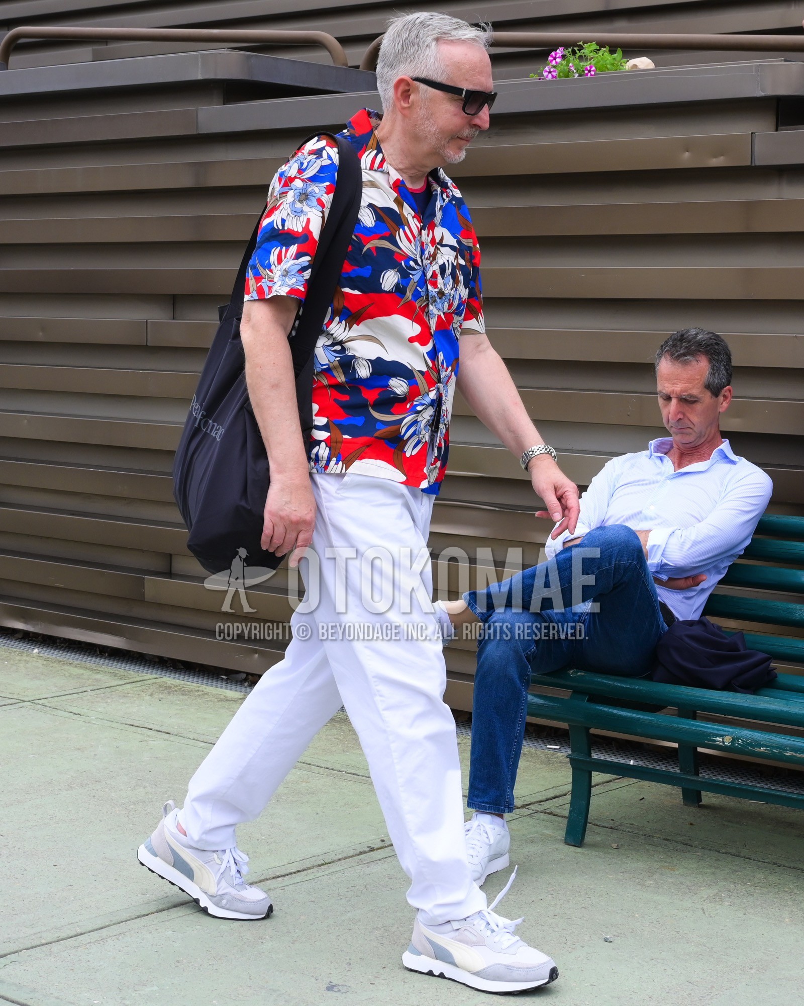 Men's spring summer outfit with black plain sunglasses, red blue whole pattern shirt, white plain slacks, white low-cut sneakers, black plain shoulder bag.