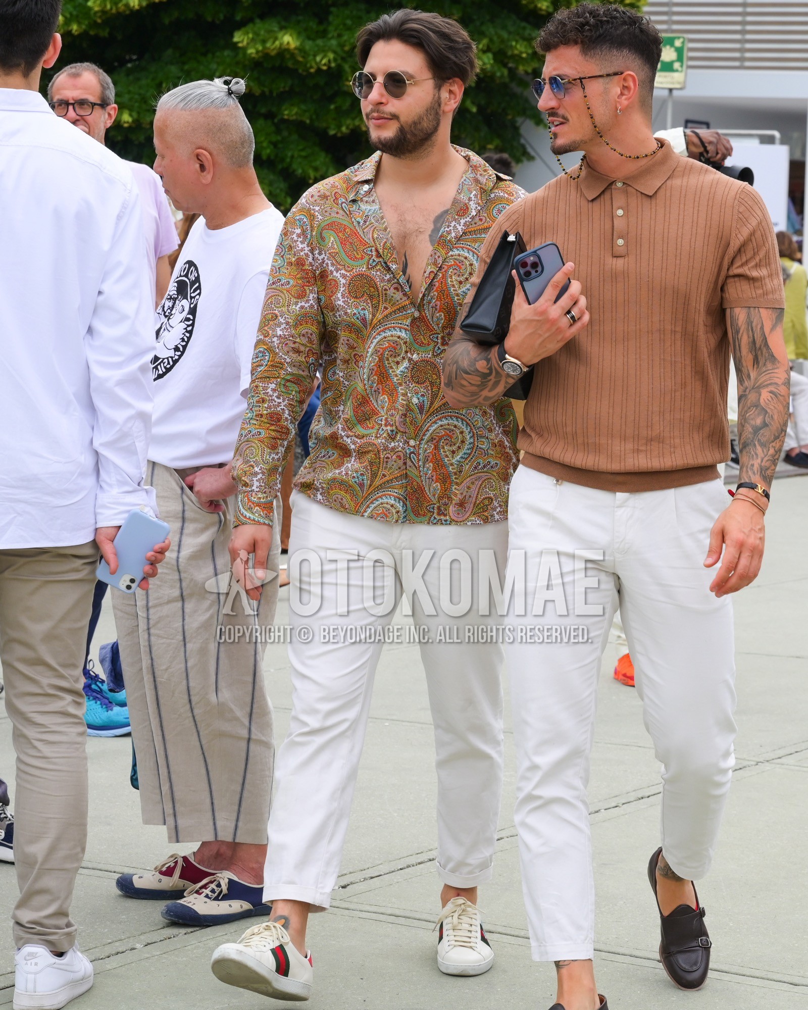 Men's spring summer autumn outfit with black plain sunglasses, beige paisley shirt, white plain chinos, white low-cut sneakers.