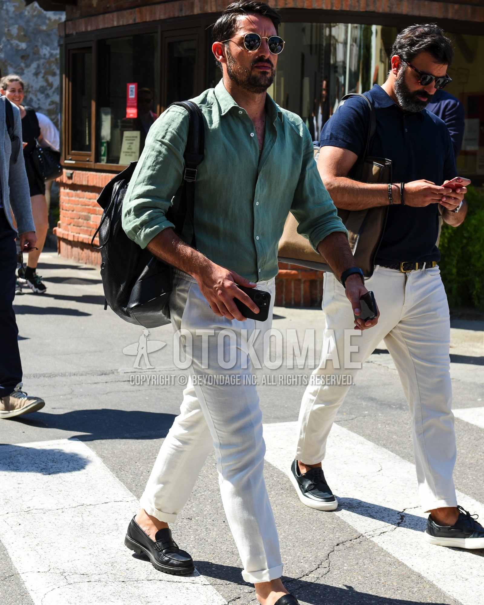 Men's spring summer outfit with gold plain sunglasses, green plain shirt, white plain easy pants, black coin loafers leather shoes, black plain backpack.