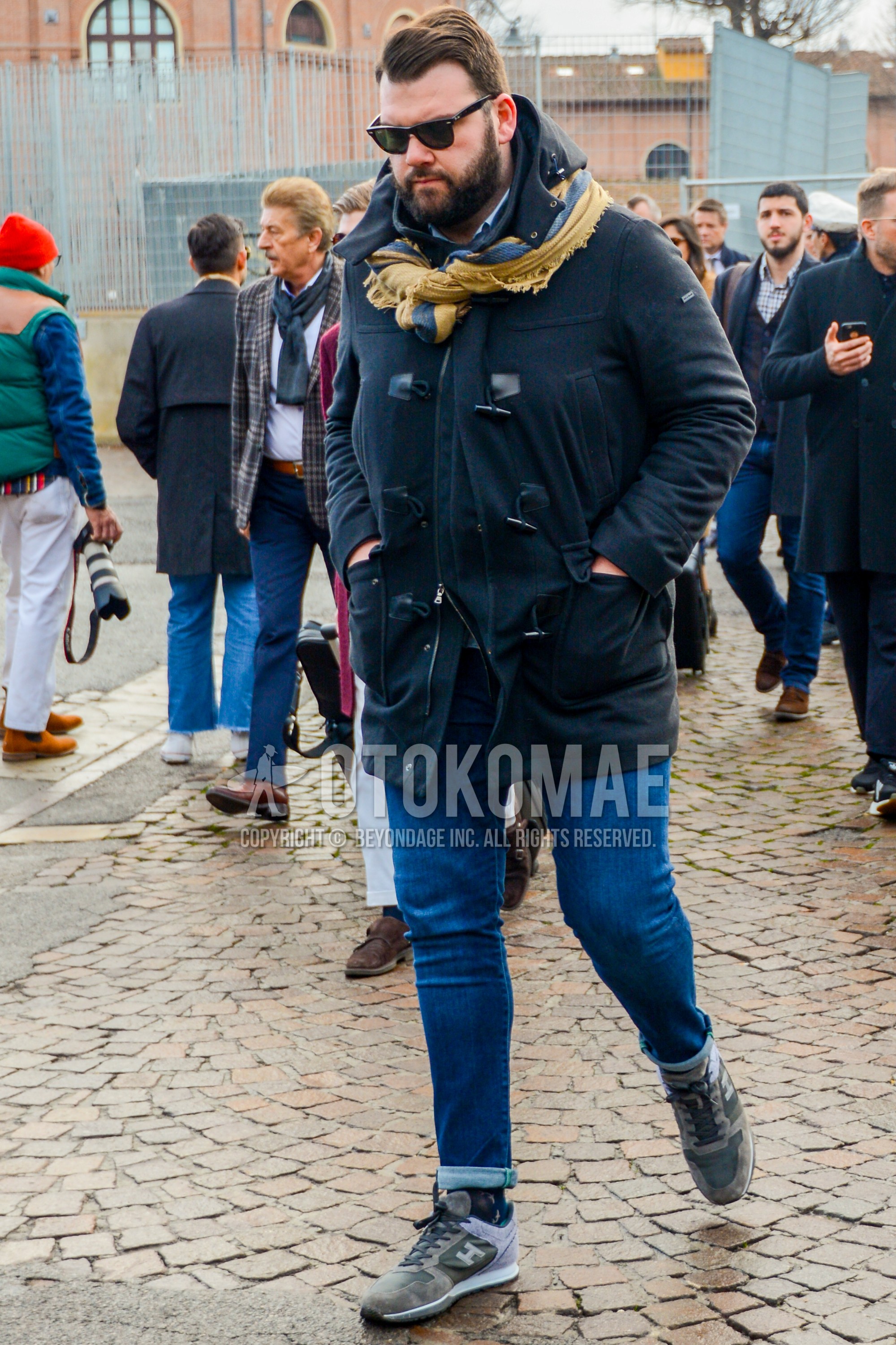 Men's winter outfit with plain sunglasses, yellow plain scarf, black plain duffle coat, blue plain denim/jeans, dark gray plain socks, gray low-cut sneakers.