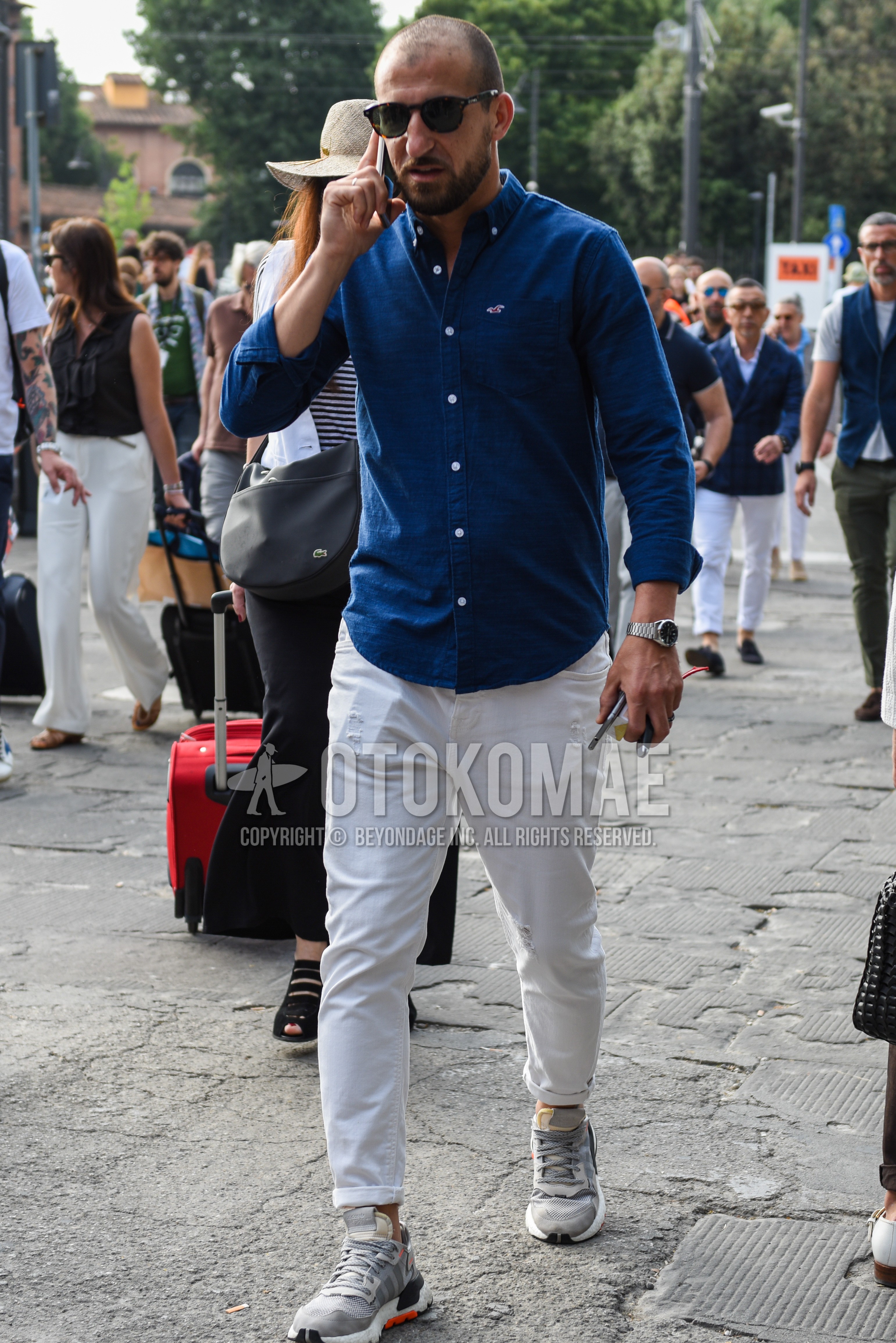Men's spring summer outfit with brown tortoiseshell sunglasses, blue plain shirt, white plain cotton pants, gray low-cut sneakers.