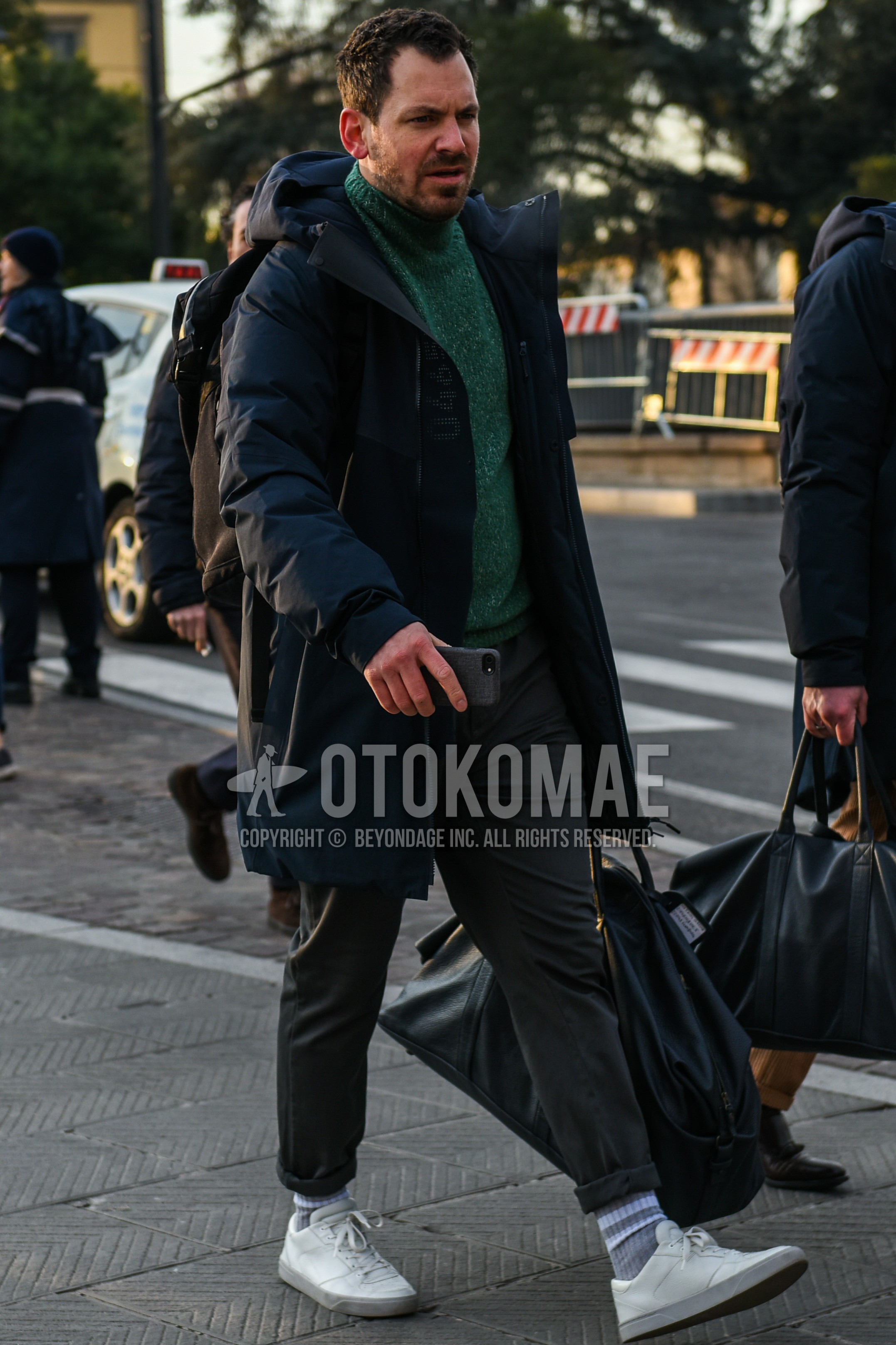 Men's winter outfit with navy plain down jacket, navy plain hooded coat, green plain turtleneck knit, gray plain cotton pants, gray plain socks, white low-cut sneakers, black plain briefcase/handbag.