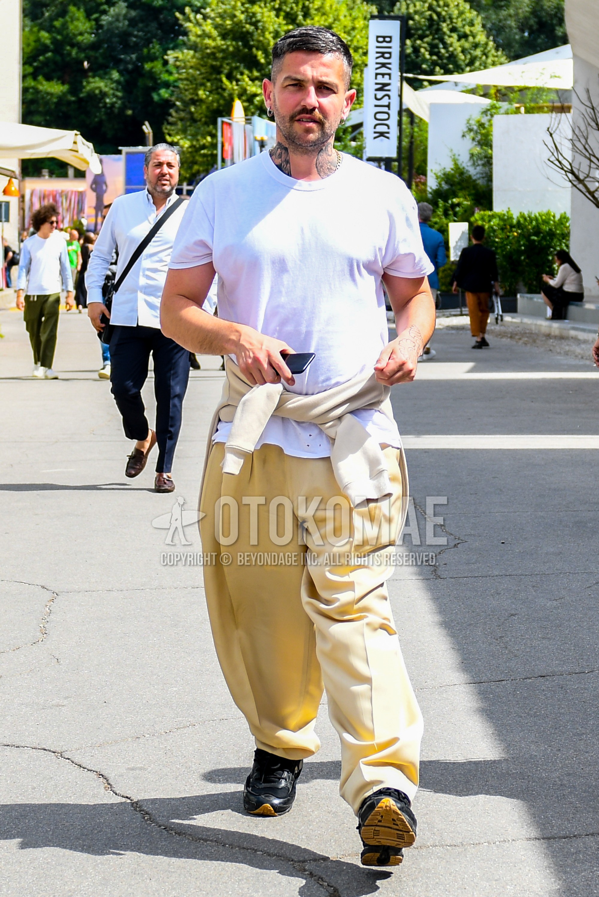 Men's summer outfit with white plain t-shirt, beige plain wide pants, black sneakers.