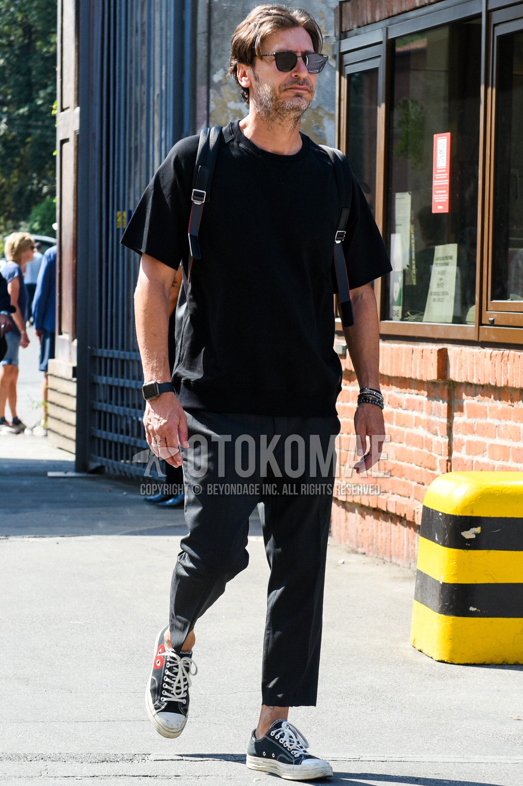 Men's spring summer outfit with black plain sunglasses, black plain t-shirt, black plain denim/jeans, black low-cut sneakers, black plain backpack.