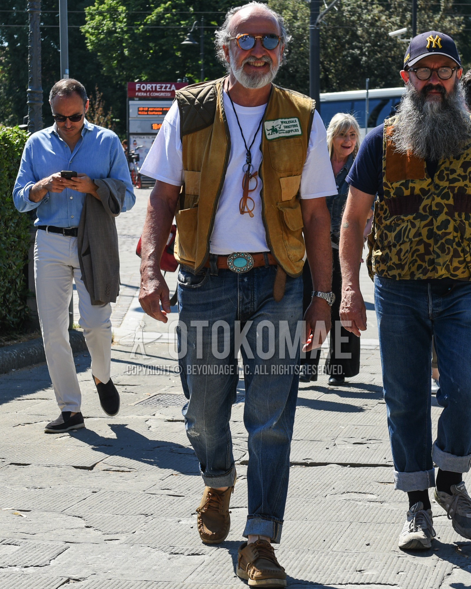 Men's spring summer outfit with brown tortoiseshell sunglasses, brown plain casual vest, white plain t-shirt, brown plain leather belt, blue plain denim/jeans, beige moccasins/deck shoes leather shoes.