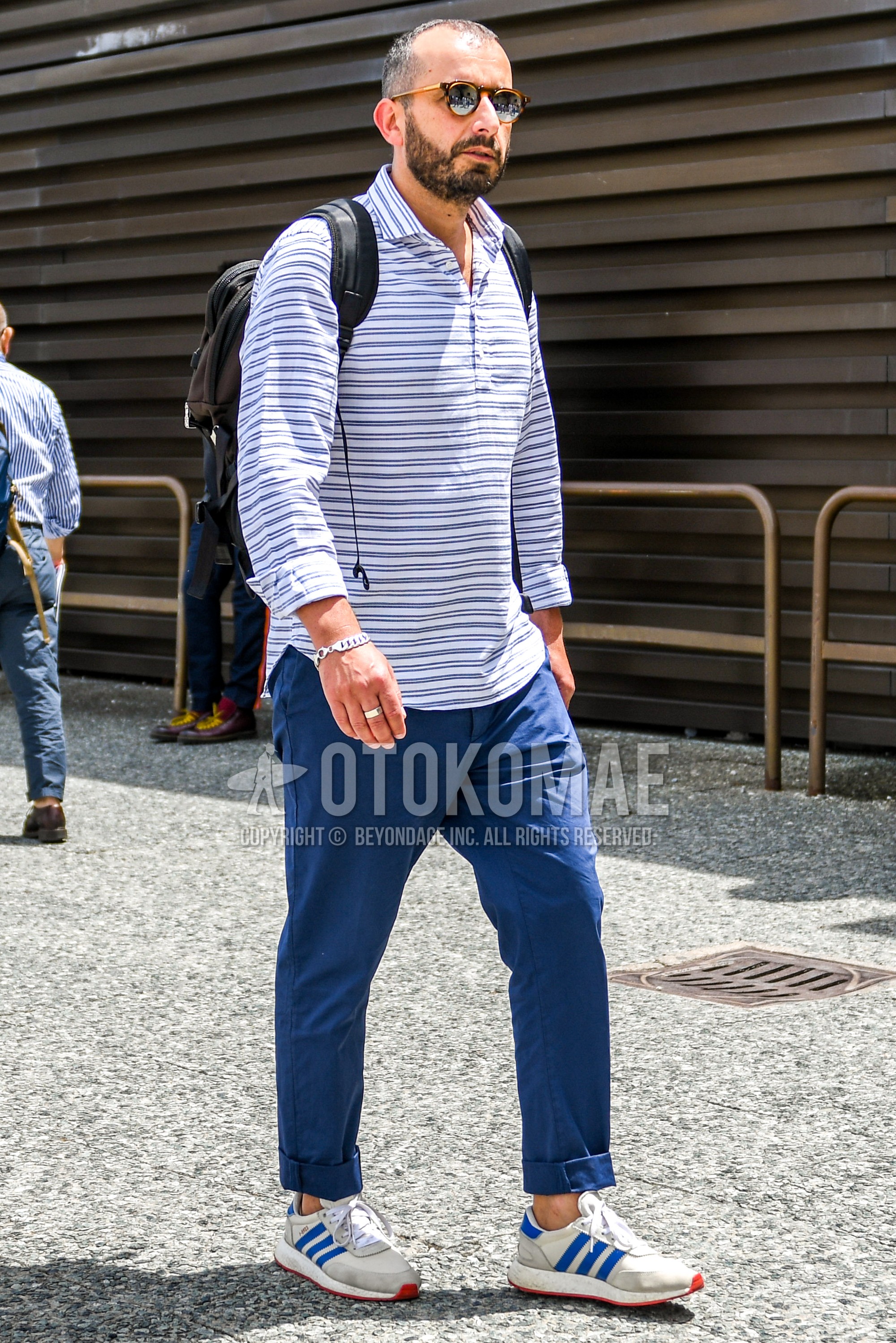 Men's spring summer autumn outfit with plain sunglasses, white navy horizontal stripes shirt, navy plain chinos, white low-cut sneakers.