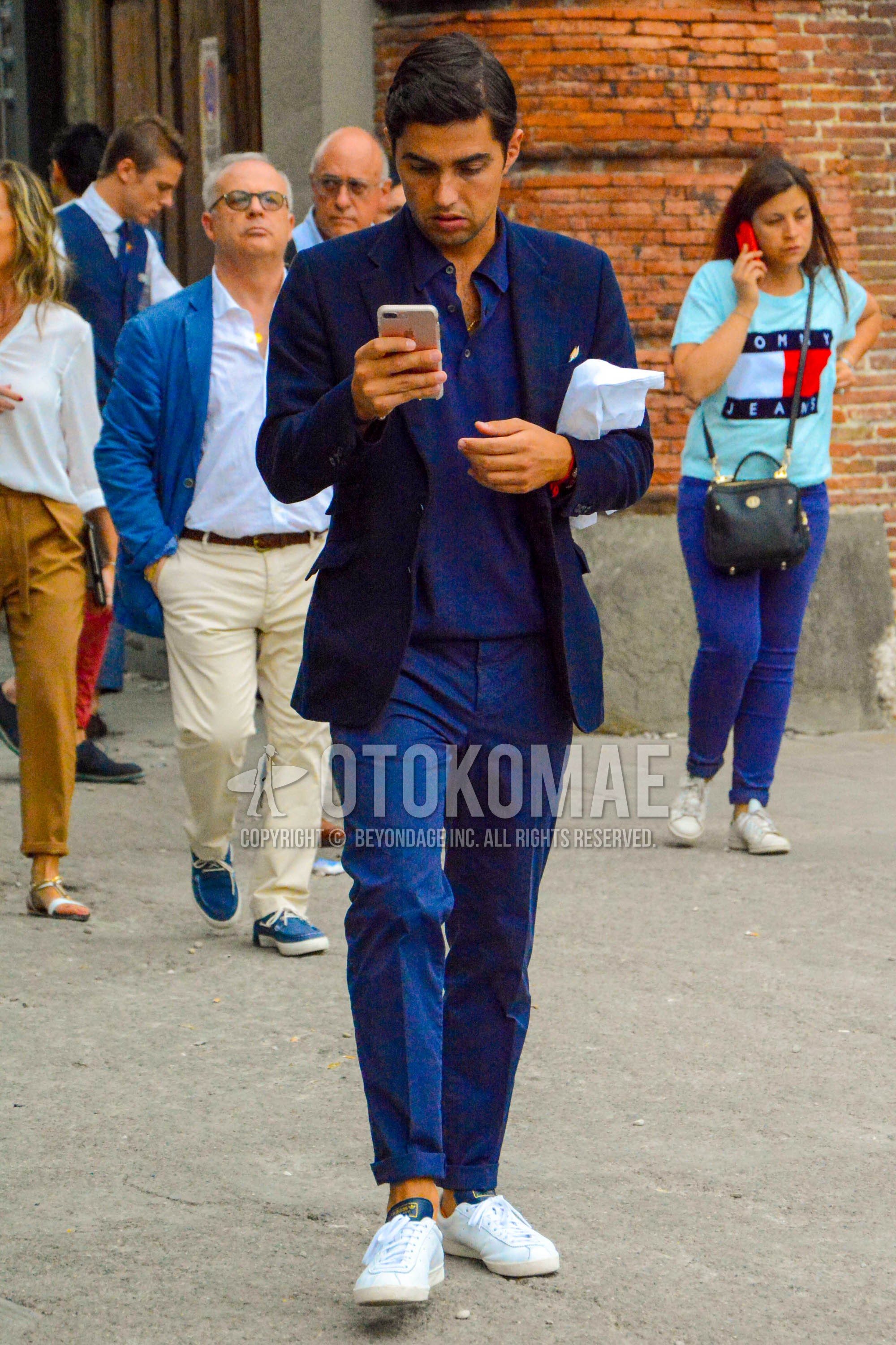 Men's spring summer autumn outfit with navy plain tailored jacket, navy plain polo shirt, navy plain slacks, white low-cut sneakers.