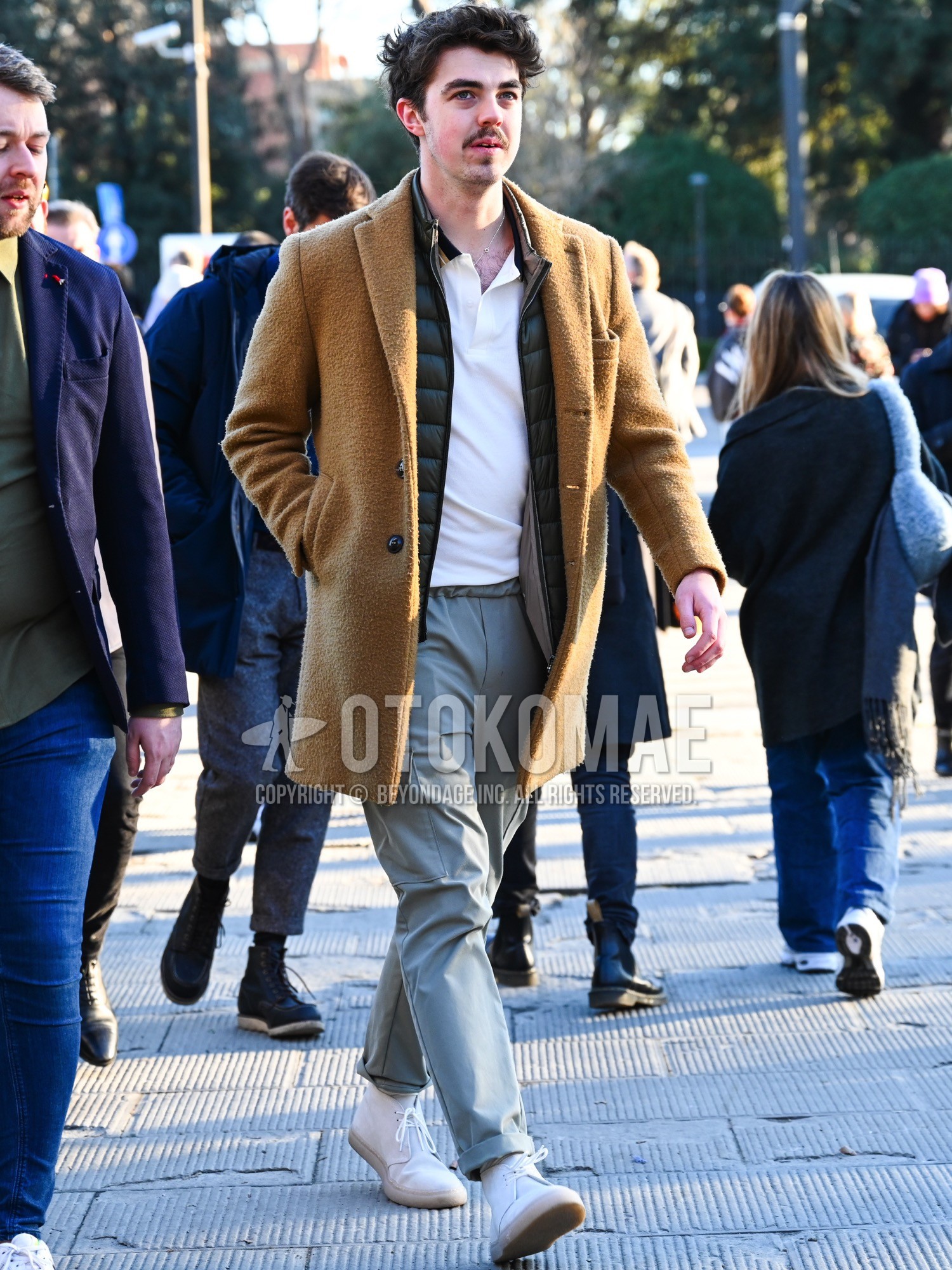 Men's autumn winter outfit with brown beige plain chester coat, olive green plain down jacket, white plain shirt, gray plain cargo pants, white chukka boots.