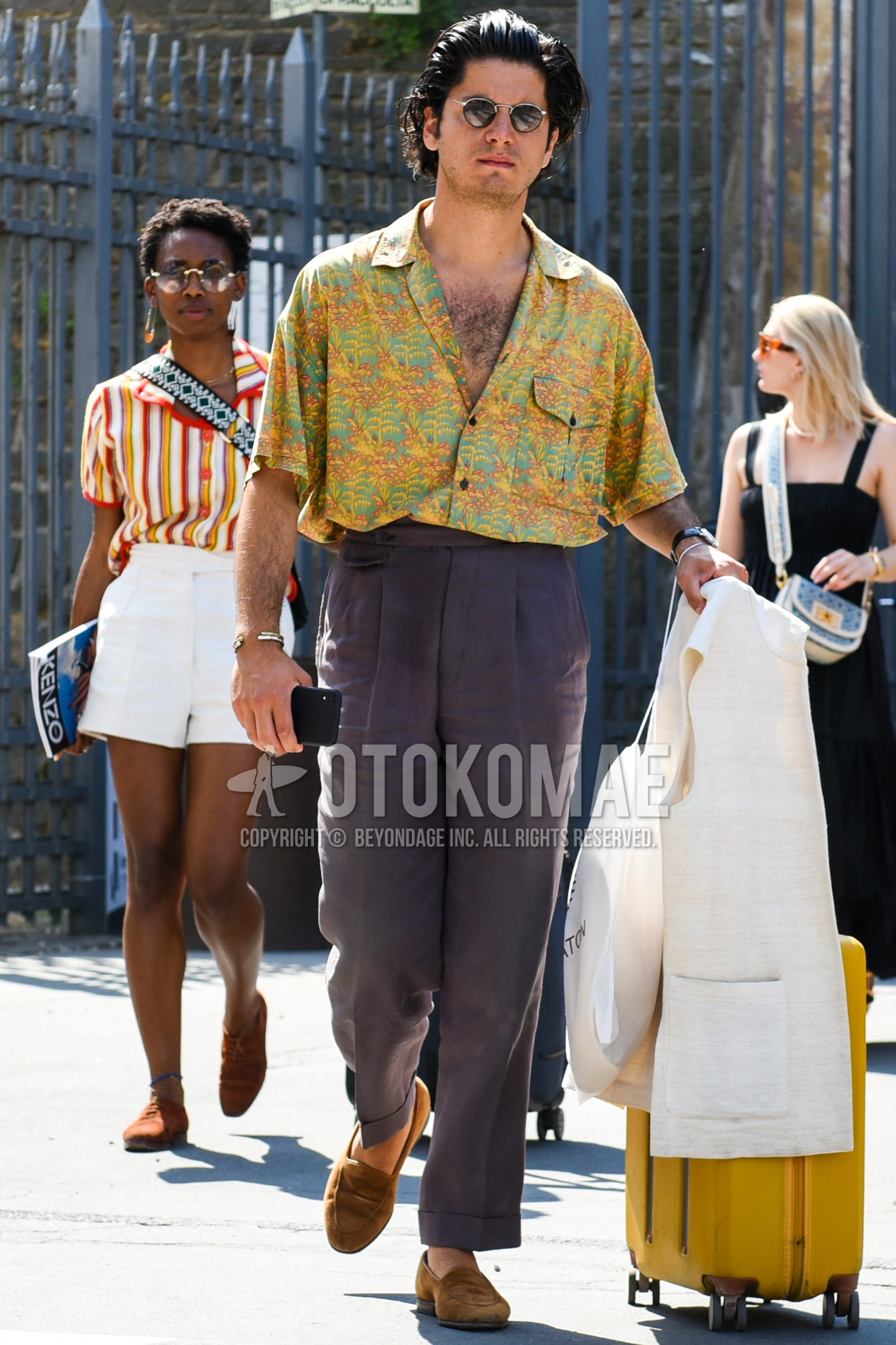 Men's spring summer outfit with black plain sunglasses, yellow green tops/innerwear shirt, white plain gilet, purple plain beltless pants, brown coin loafers leather shoes, yellow plain suitcase.
