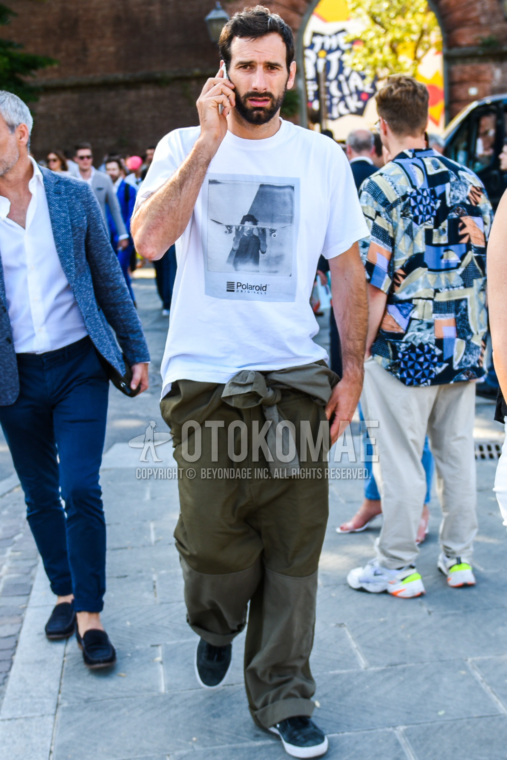 Men's summer outfit with white graphic t-shirt, olive green plain wide pants, blue low-cut sneakers.