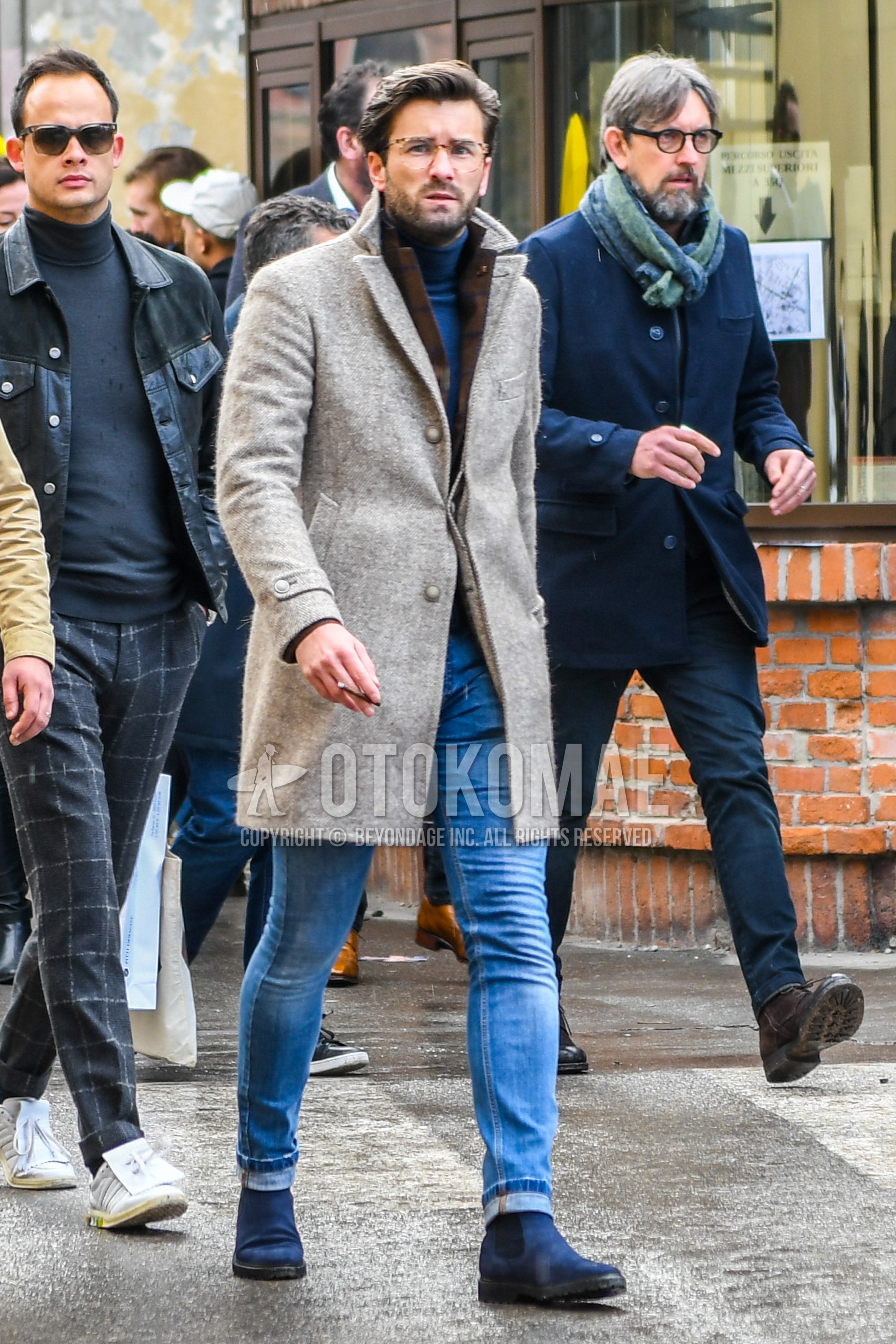 Men's winter outfit with plain glasses, brown plain chester coat, brown check tailored jacket, blue plain turtleneck knit, blue plain denim/jeans, navy side-gore boots.