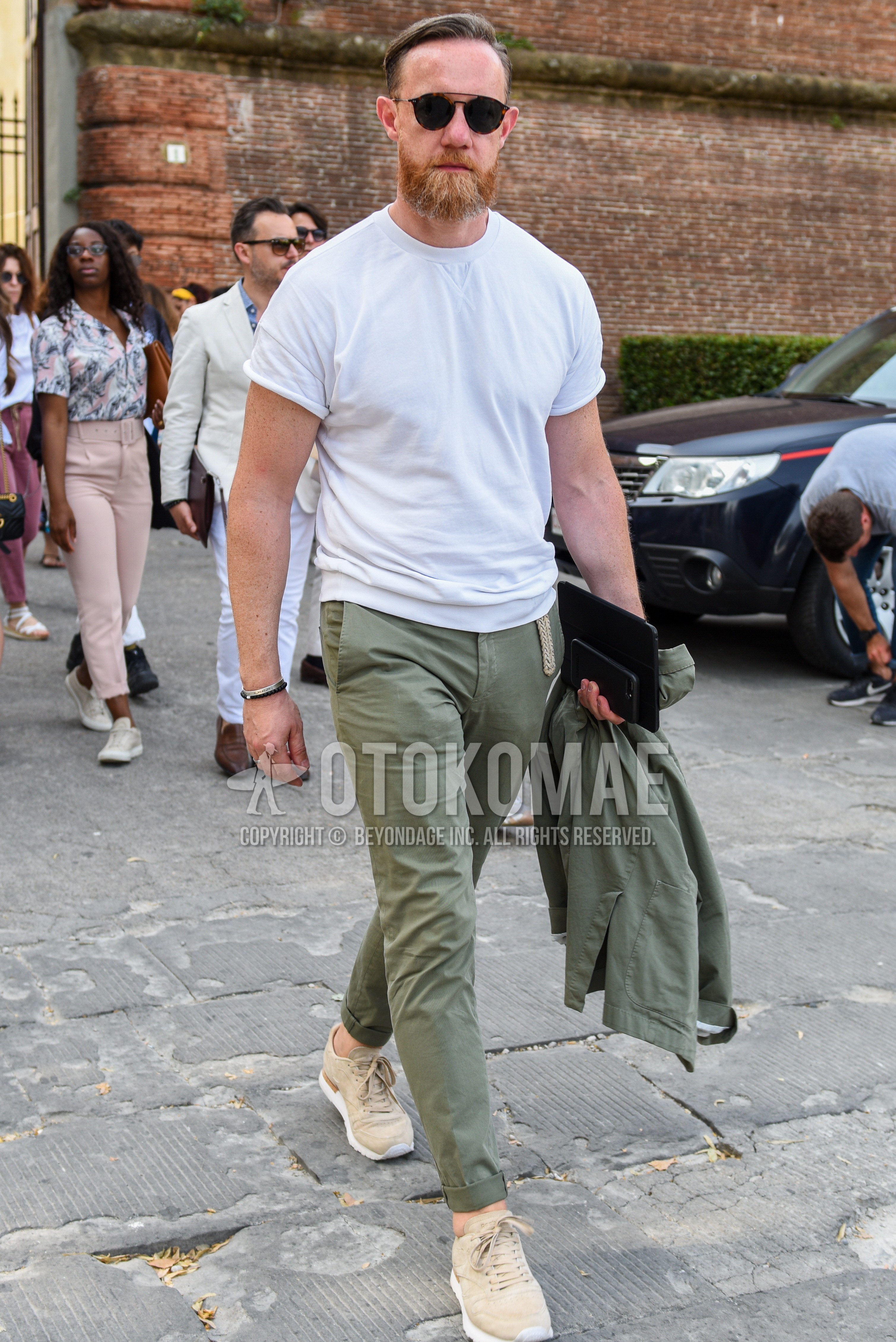 Men's summer outfit with black tortoiseshell sunglasses, white plain t-shirt, olive green plain chinos, beige low-cut sneakers.