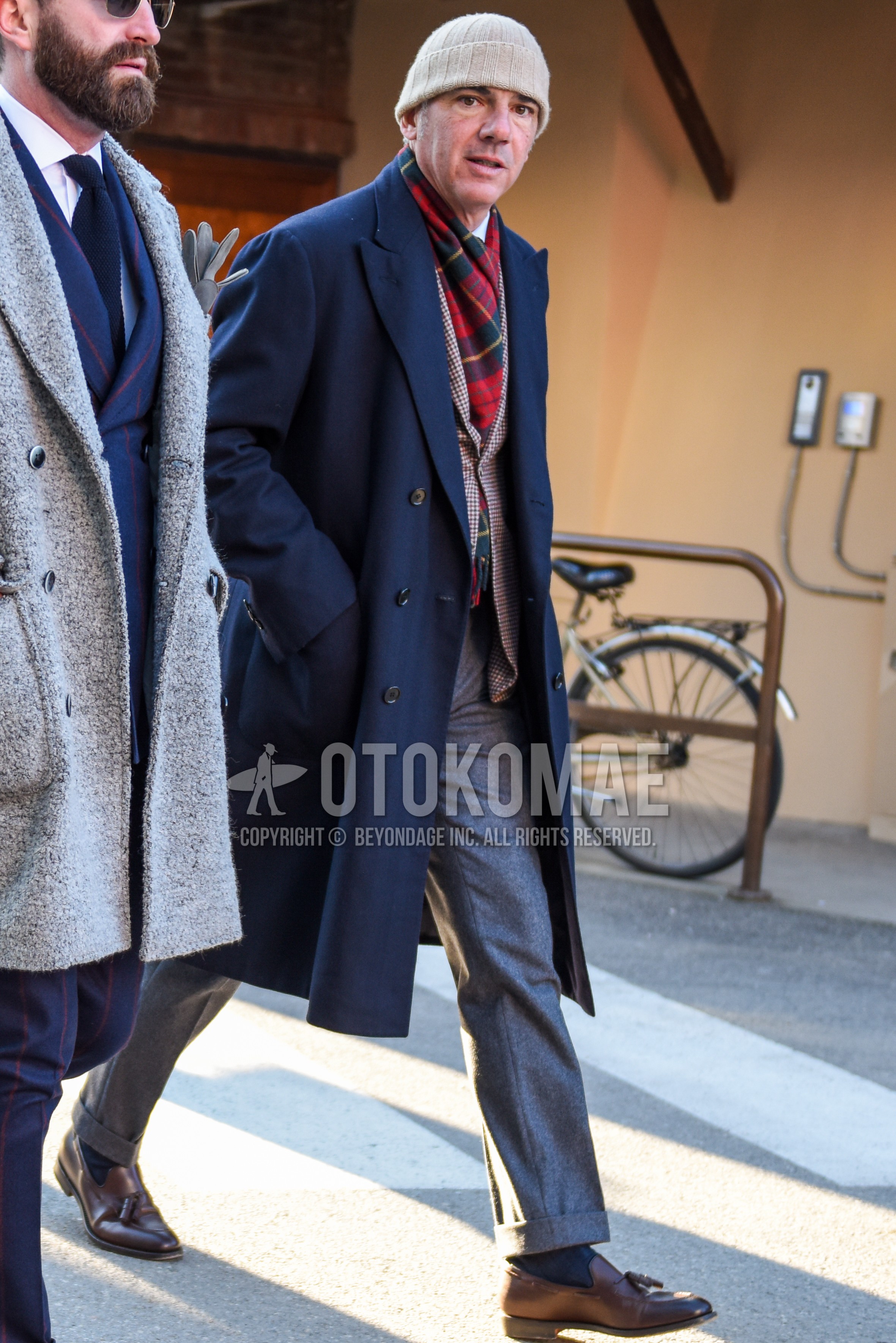 Men's autumn winter outfit with beige plain knit cap, red black check scarf, navy plain chester coat, brown check tailored jacket, gray plain slacks, gray plain ankle pants, dark gray plain socks, brown tassel loafers leather shoes.