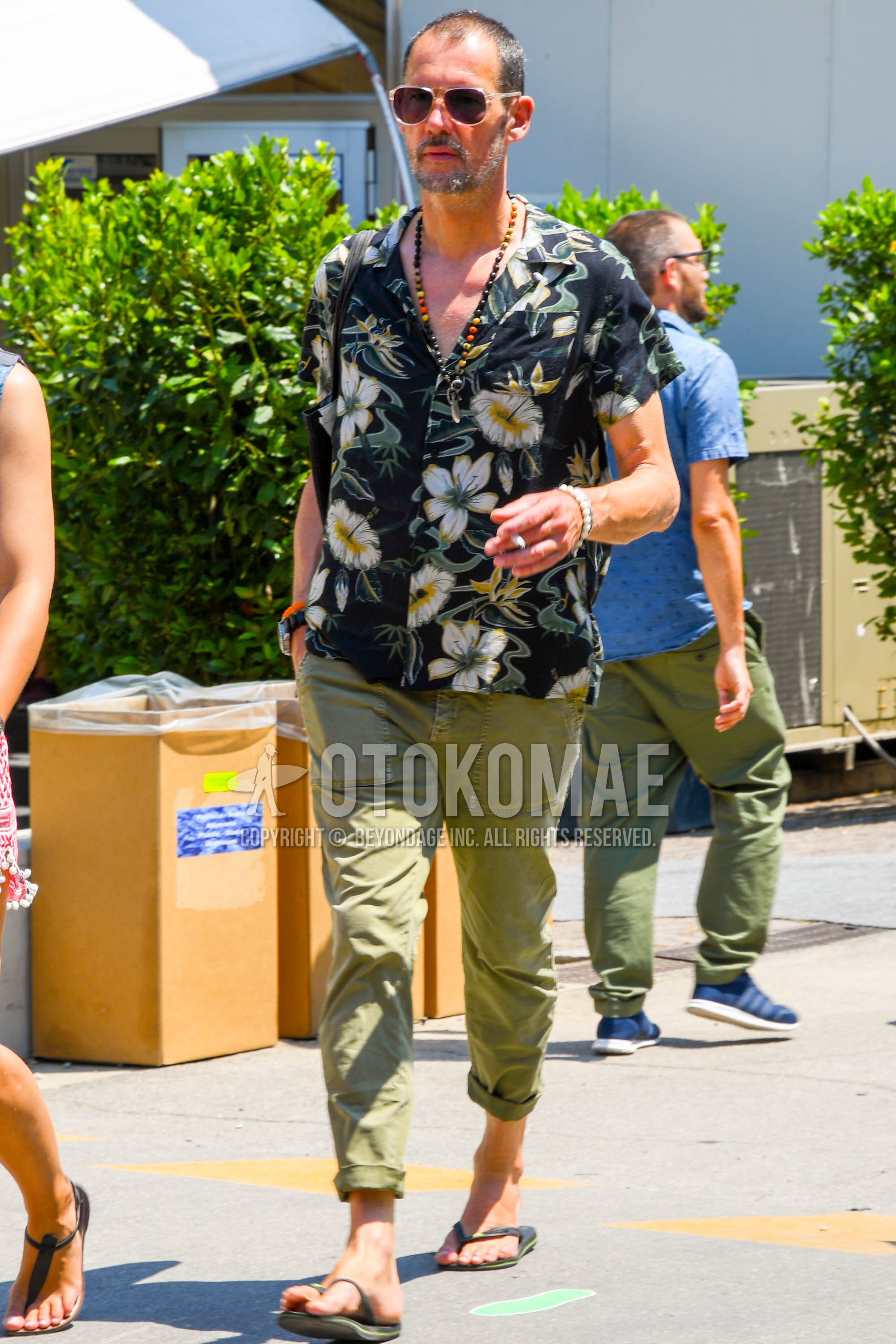 Men's summer outfit with clear plain sunglasses, black botanical shirt, olive green plain chinos, black flip flops sandals.