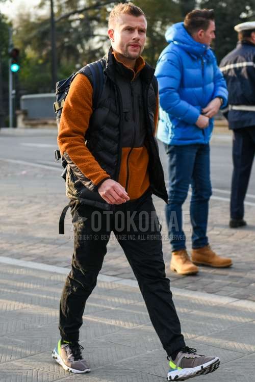 ブラウン・黒無地のフリースジャケット、黒無地のカジュアルベスト、黒無地のジョガーパンツ/リブパンツ、ナイキ リアクトエレメント のグレーローカットのスニーカー、黒無地のバックパックを合わせた秋冬のメンズコーデ・着こなし。