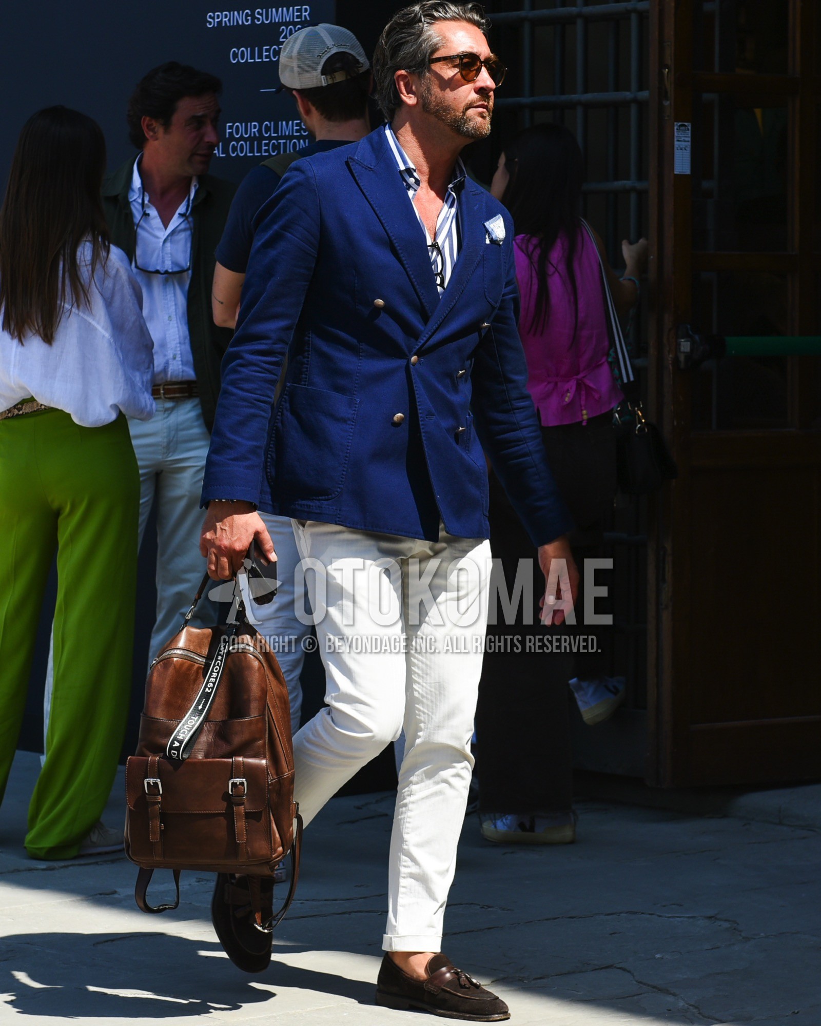 Men's spring summer outfit with brown tortoiseshell sunglasses, navy plain tailored jacket, navy white stripes shirt, white plain cotton pants, brown tassel loafers leather shoes, brown plain backpack.