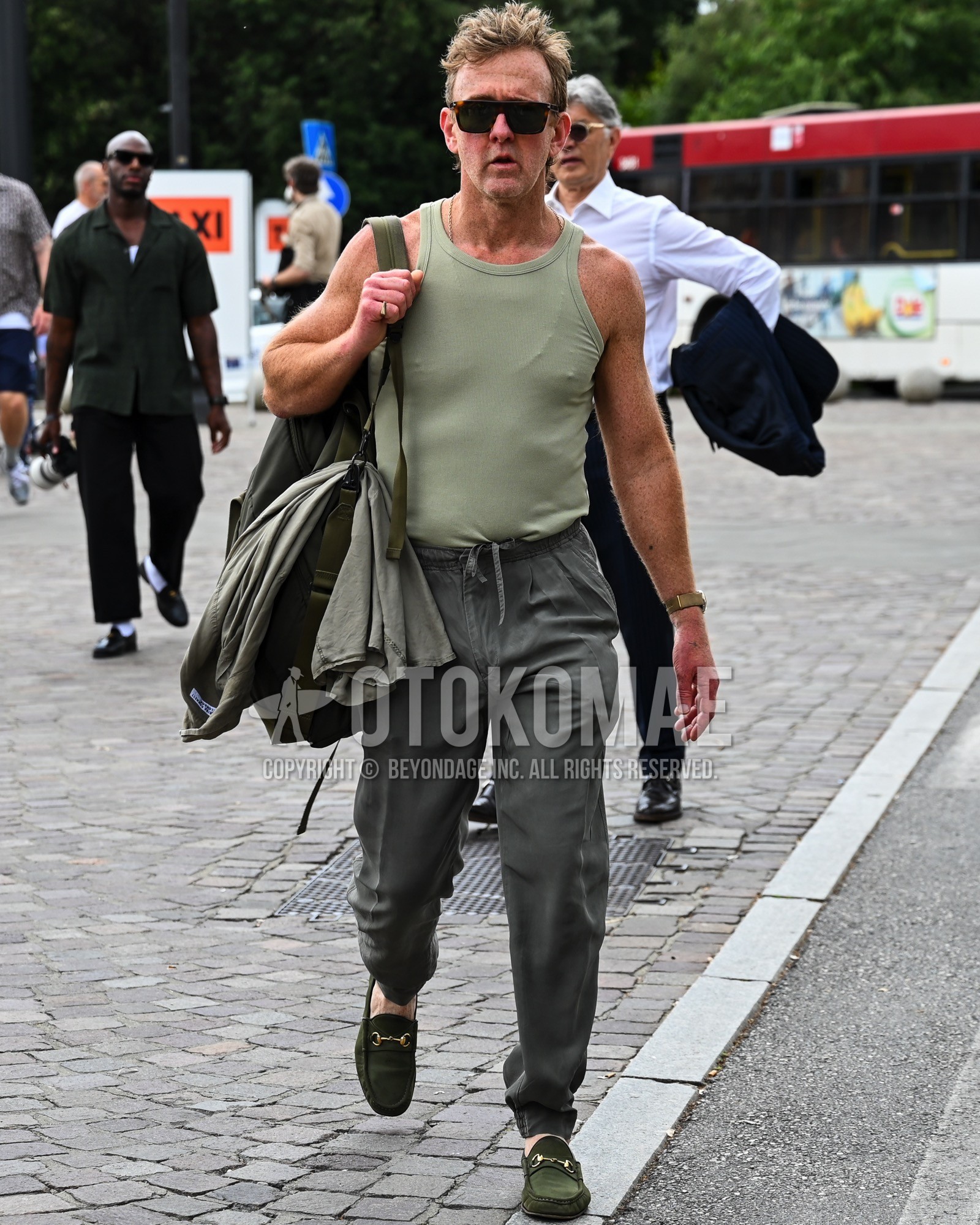Men's spring summer outfit with black plain sunglasses, green plain tank top, gray plain chinos, green bit loafers leather shoes, green plain shoulder bag.