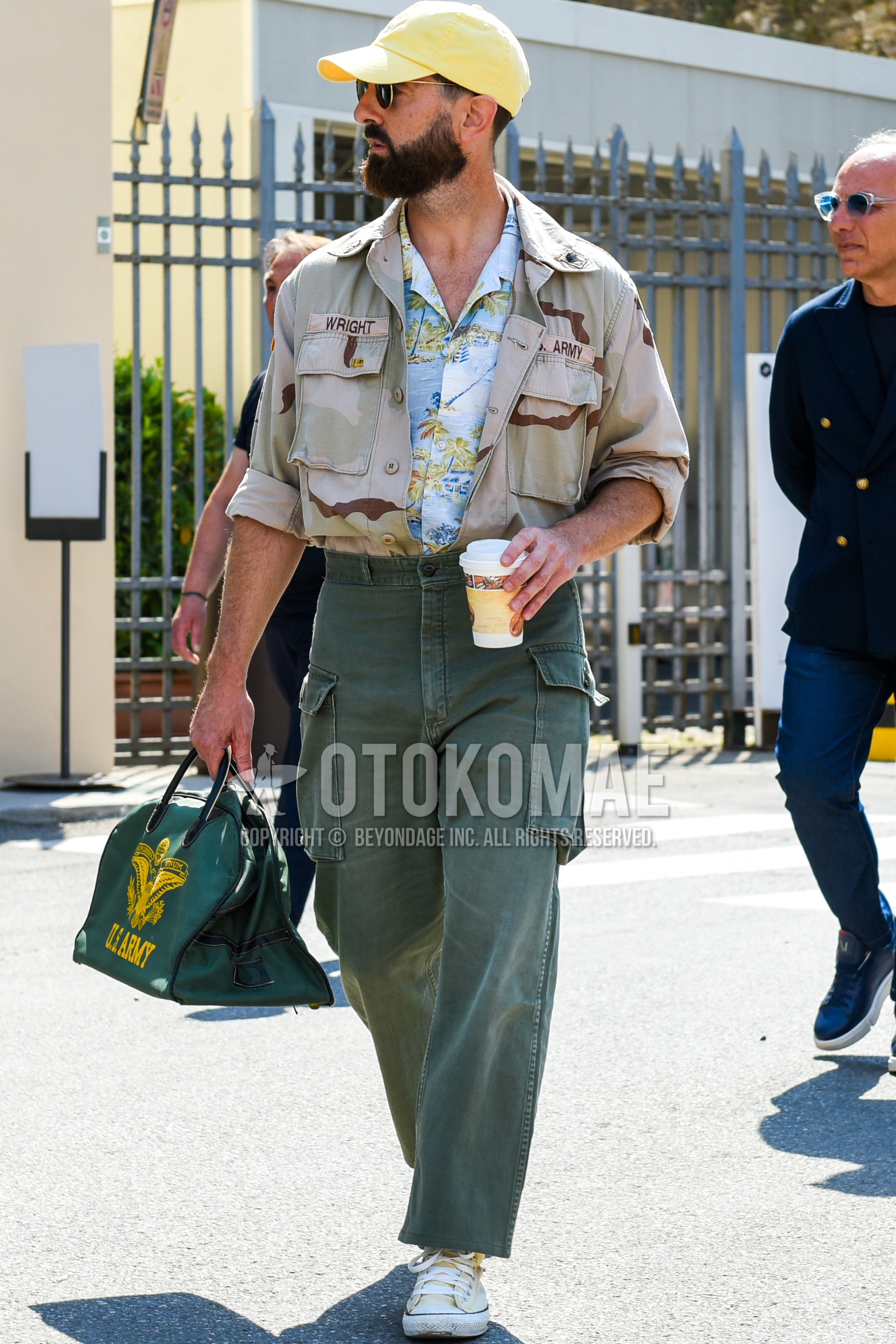 Men's spring summer autumn outfit with yellow one point baseball cap, gold plain sunglasses, beige camouflage shirt jacket, light blue tops/innerwear shirt, olive green plain cargo pants, olive green plain ankle pants, beige high-cut sneakers, olive green graphic briefcase/handbag.