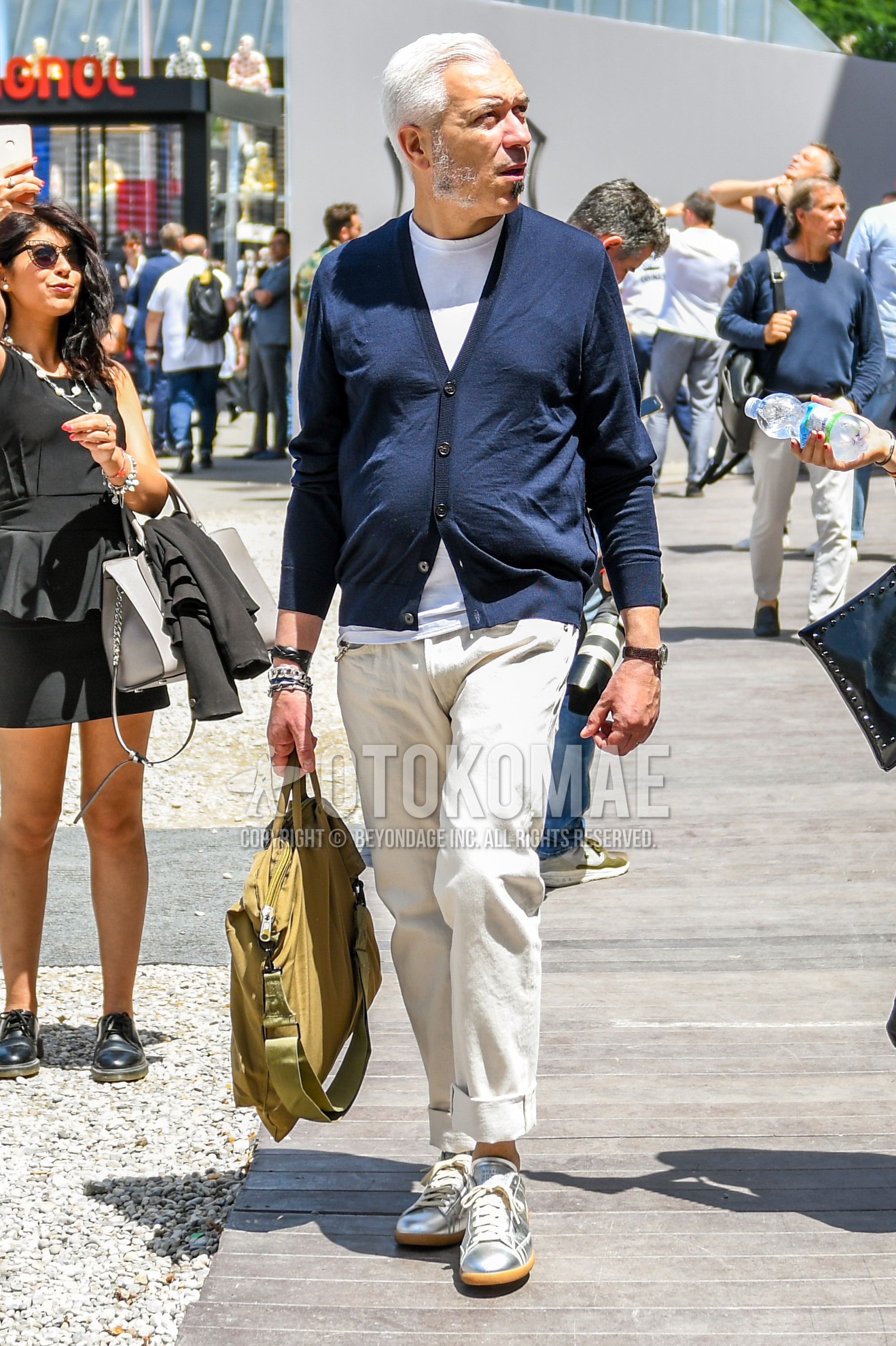Men's spring summer autumn outfit with navy plain cardigan, white plain t-shirt, beige plain chinos, silver low-cut sneakers, beige plain briefcase/handbag.