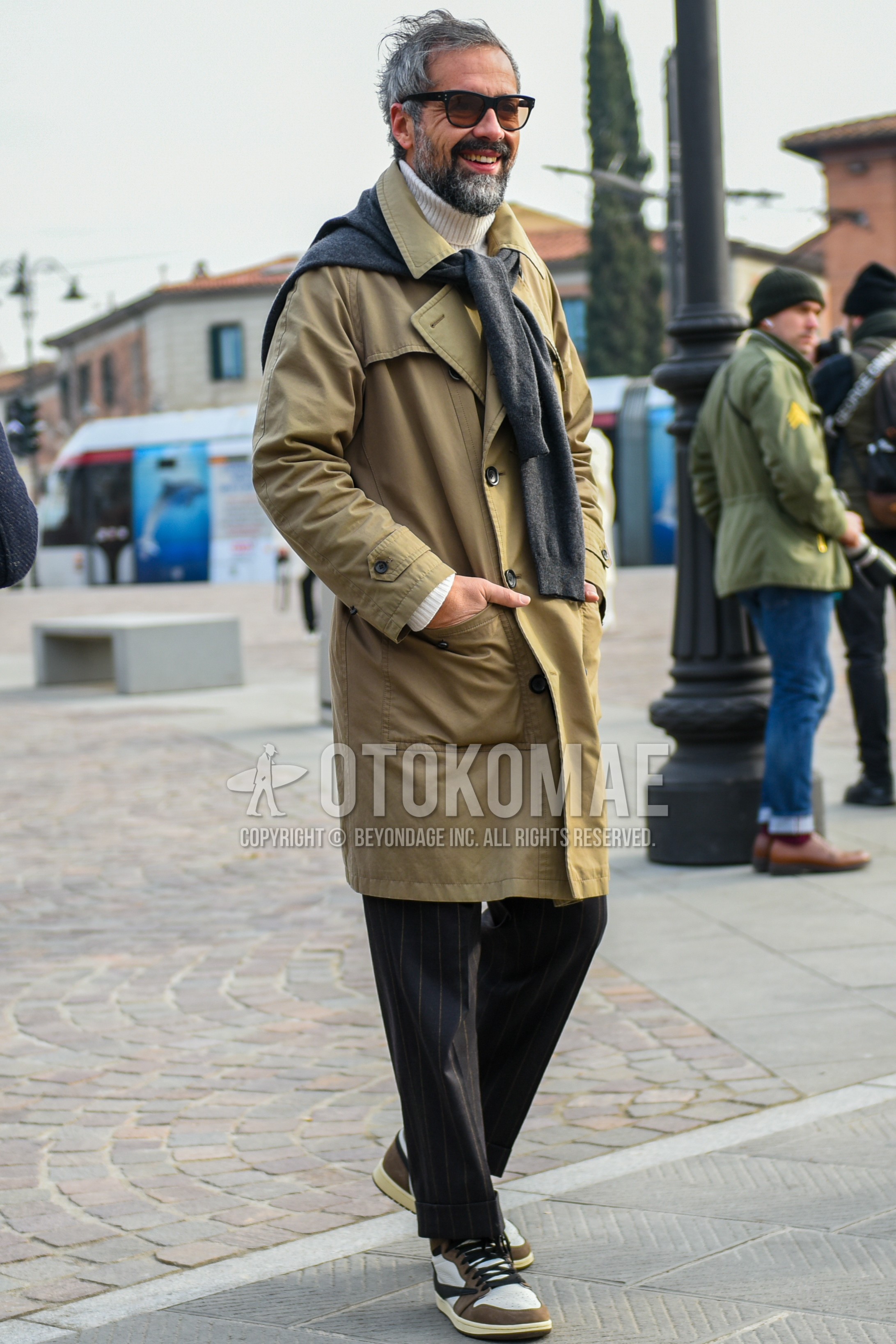 Men's autumn winter outfit with black plain sunglasses, beige plain trench coat, white plain turtleneck knit, gray plain sweater, gray stripes slacks, white brown high-cut sneakers.