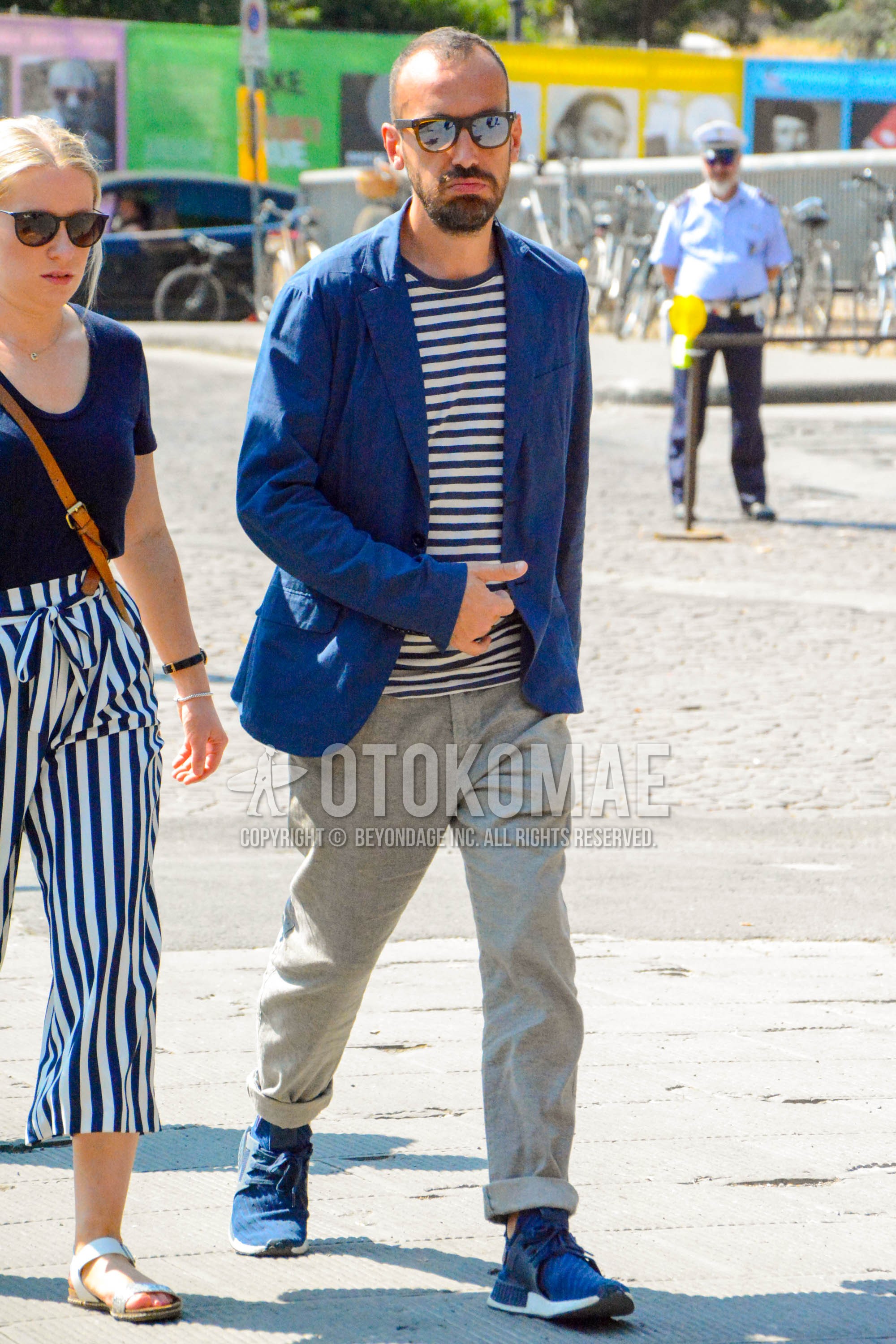 Men's spring summer autumn outfit with green plain sunglasses, navy plain tailored jacket, white navy horizontal stripes t-shirt, gray plain chinos, navy low-cut sneakers.