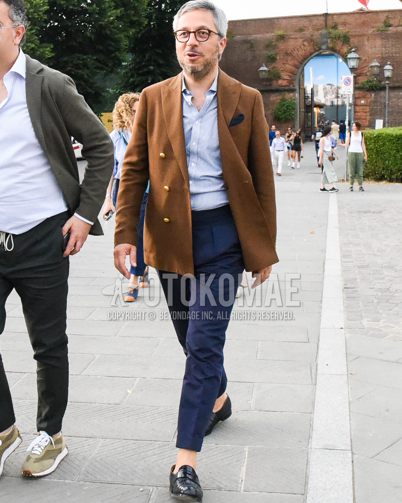 Men's spring summer autumn outfit with clear tortoiseshell glasses, brown plain tailored jacket, blue stripes shirt, navy plain slacks, navy plain pleated pants, black coin loafers leather shoes.