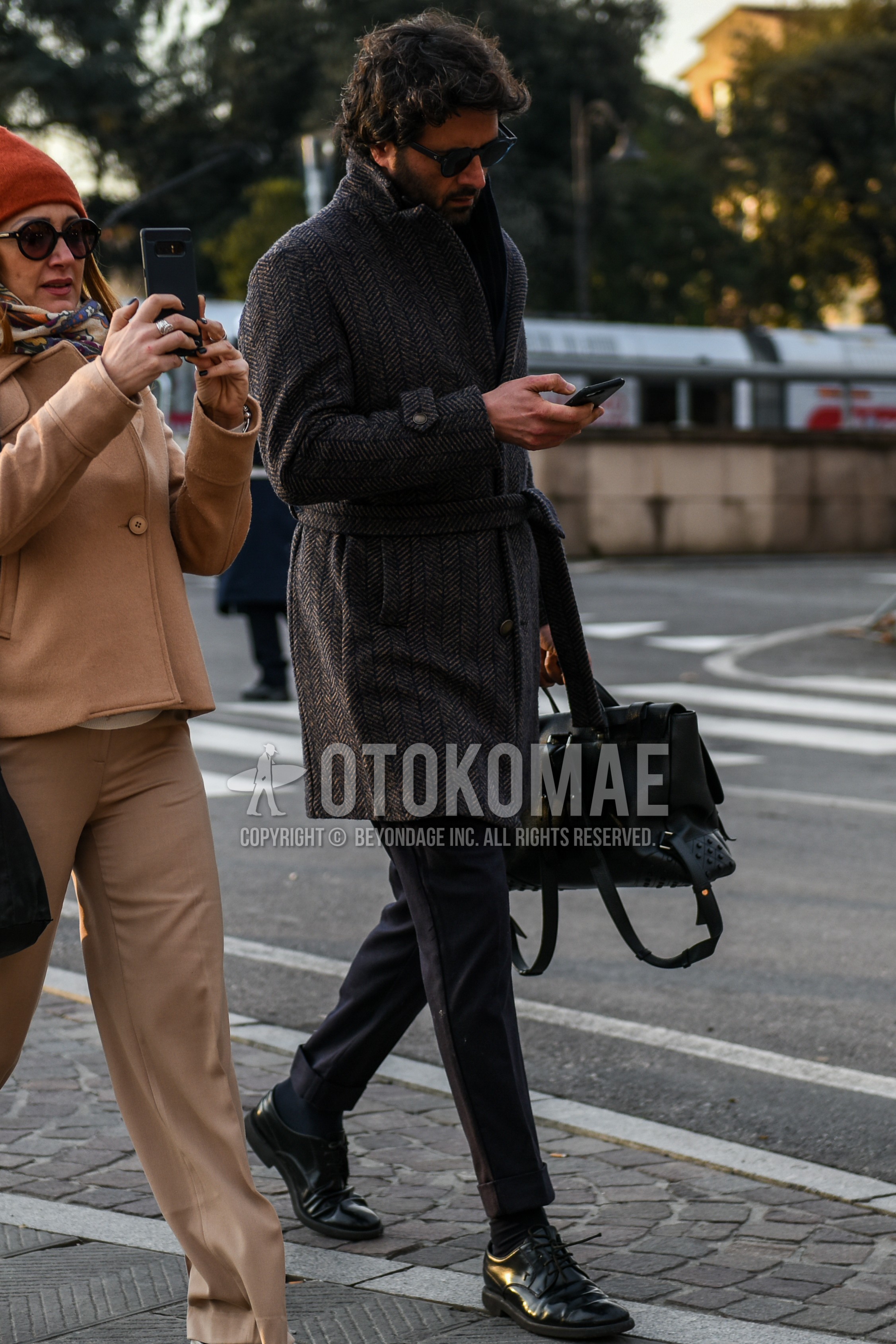 Men's autumn winter outfit with black plain sunglasses, brown herringbone belted coat, gray plain slacks, black plain socks, black plain toe leather shoes, black plain briefcase/handbag.
