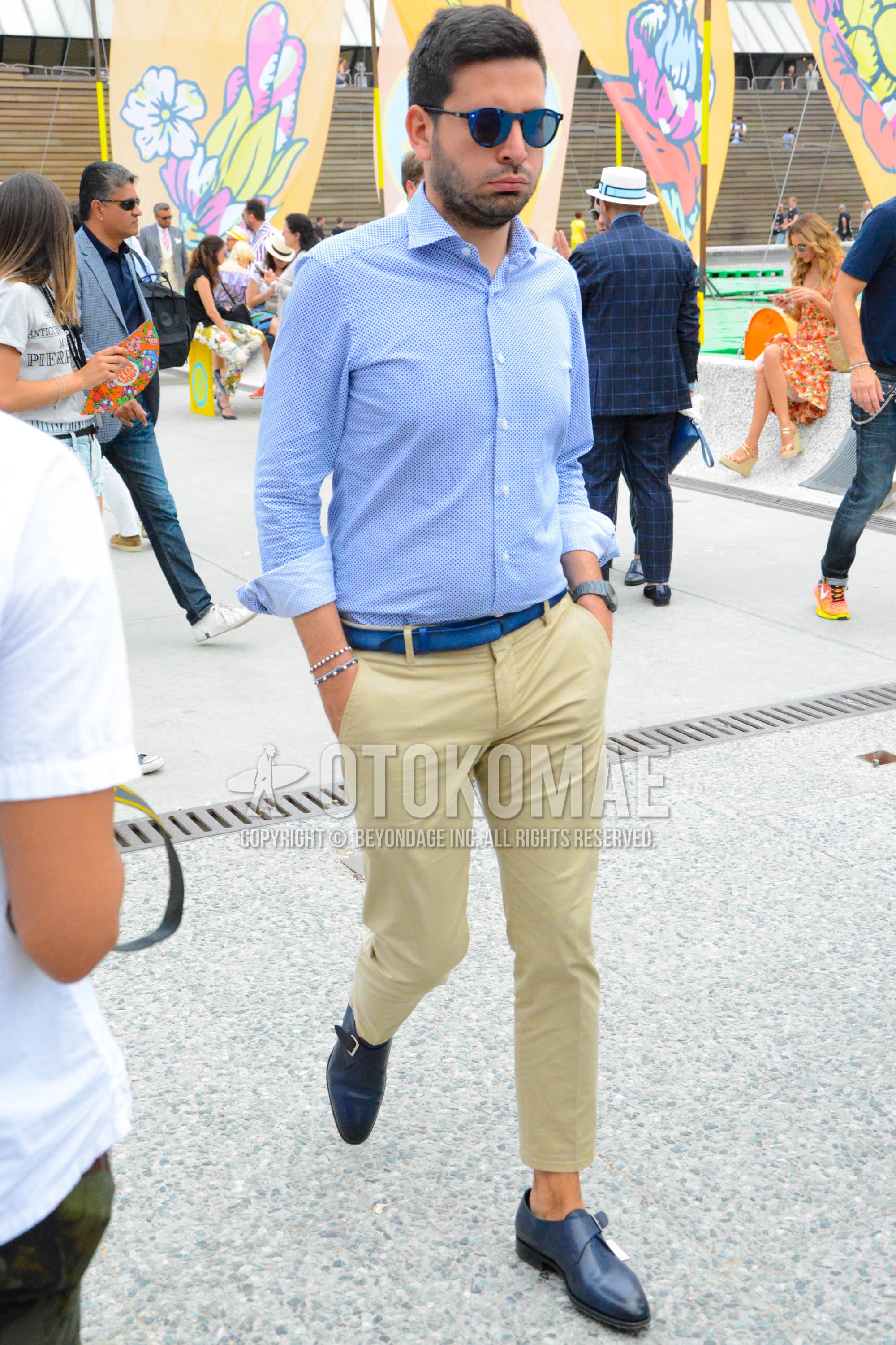 Men's spring summer outfit with blue plain sunglasses, blue plain shirt, blue plain leather belt, beige plain chinos, navy monk shoes leather shoes.