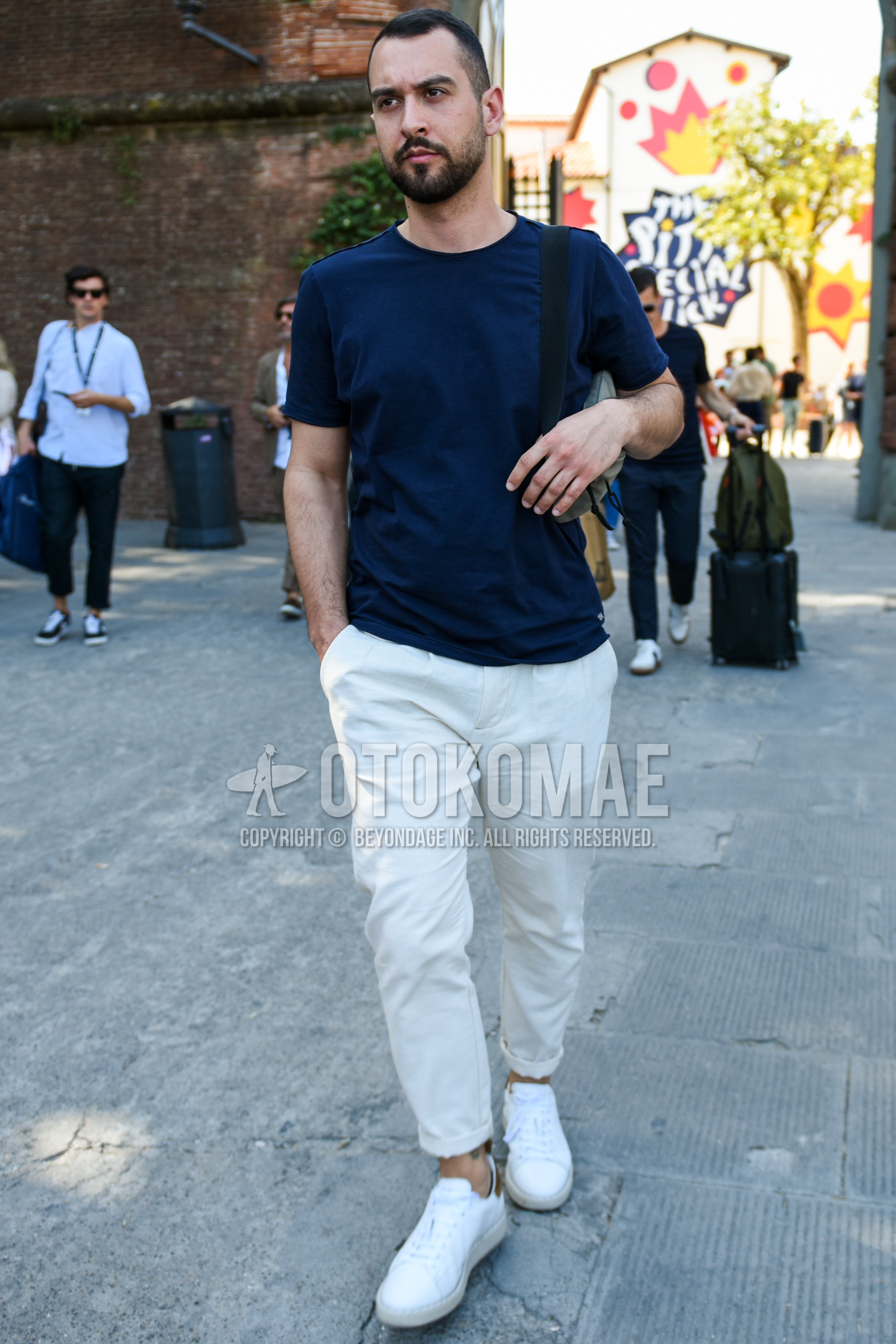 Men's summer outfit with navy plain t-shirt, white plain cotton pants, white low-cut sneakers.