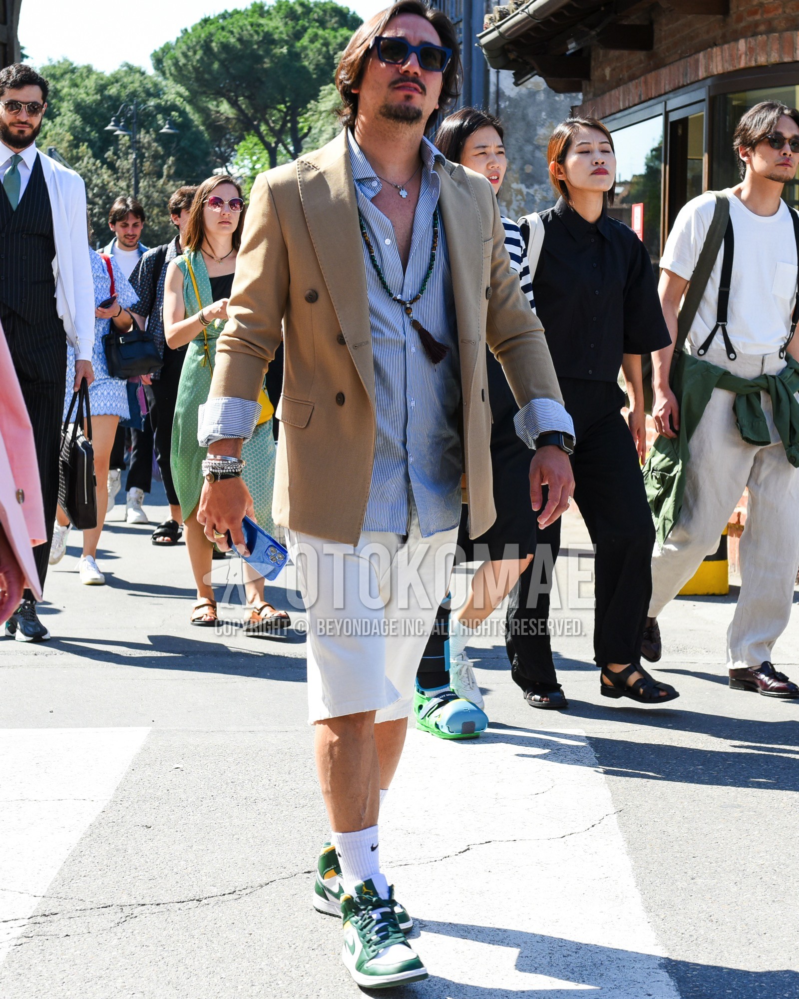 Men's spring summer outfit with navy plain sunglasses, beige plain tailored jacket, white blue stripes cardigan, white plain short pants, white one point socks, green low-cut sneakers.