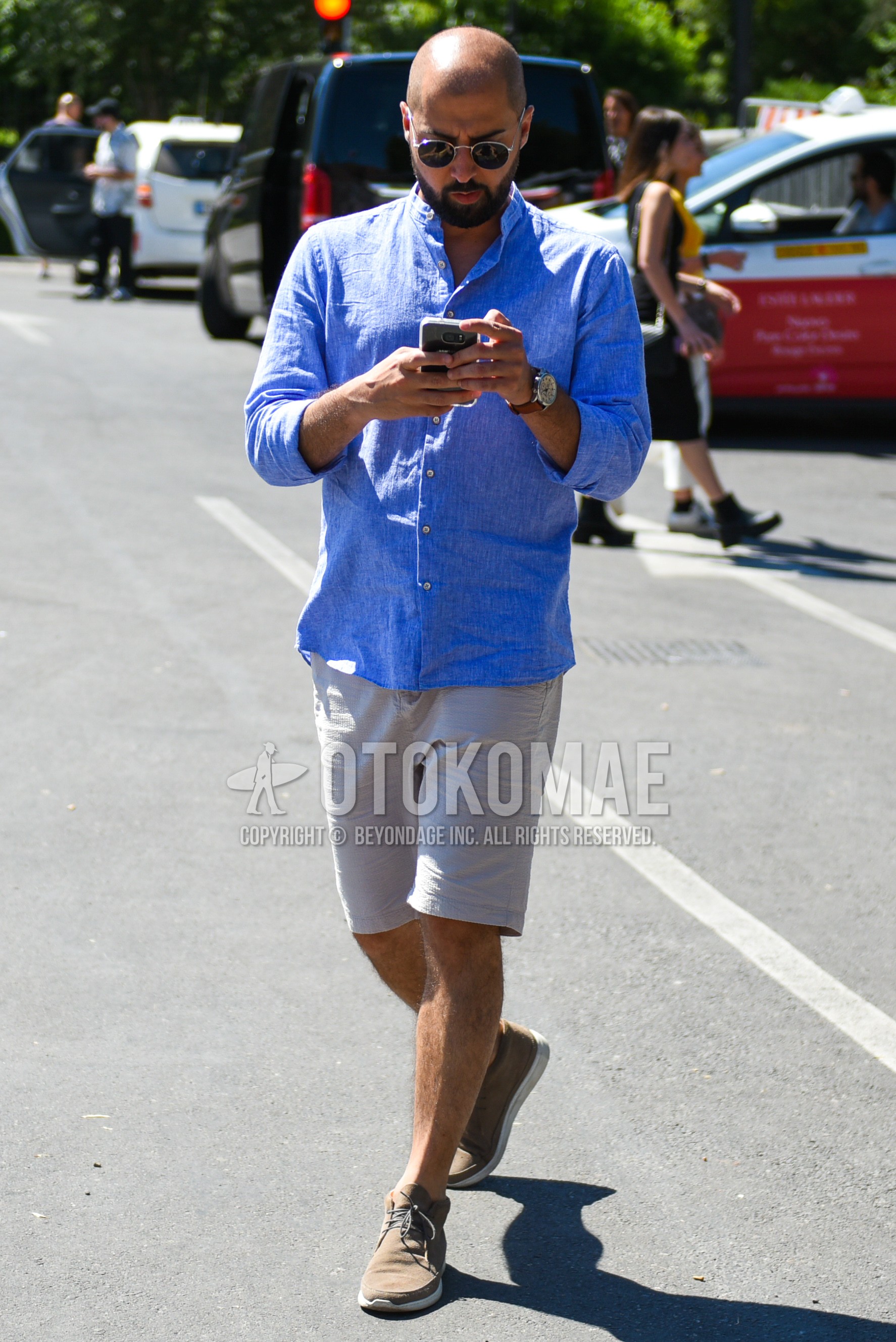 Men's spring summer outfit with silver plain sunglasses, blue plain shirt, gray white plain short pants, brown sneakers.
