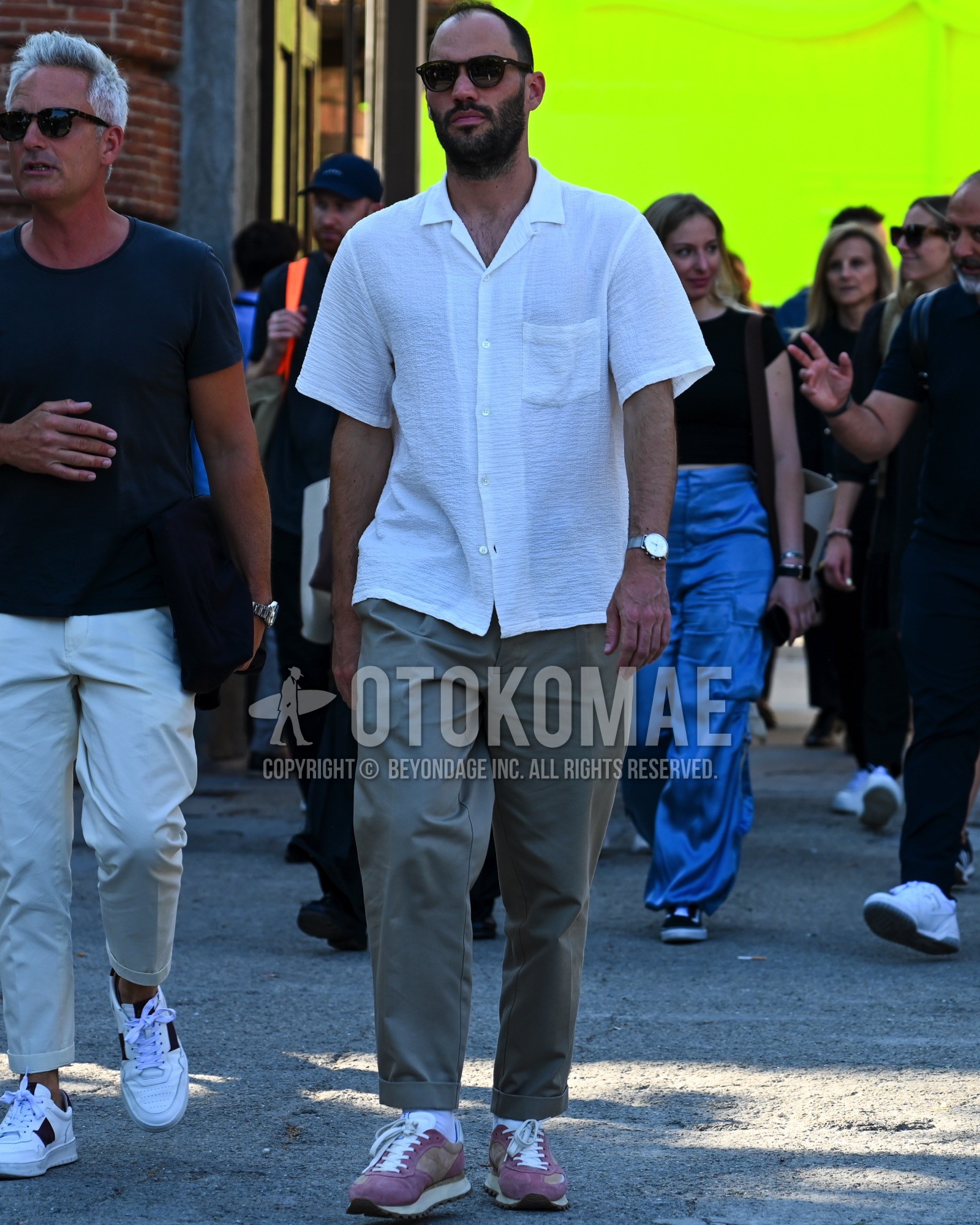 Men's spring summer outfit with black plain sunglasses, white plain shirt, beige plain chinos, pink low-cut sneakers.