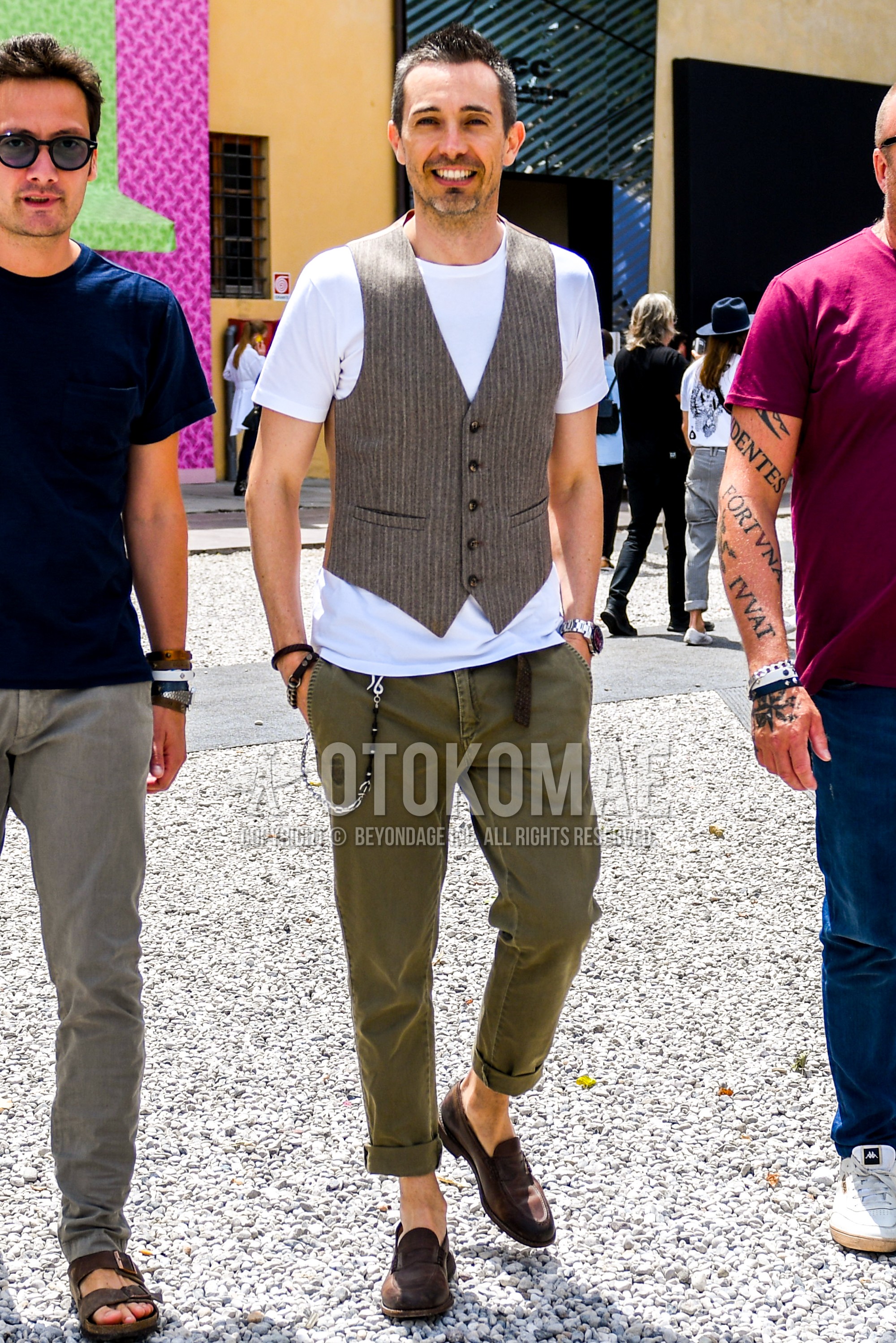 Men's summer outfit with beige stripes gilet, plain t-shirt, green plain chinos, brown coin loafers leather shoes.