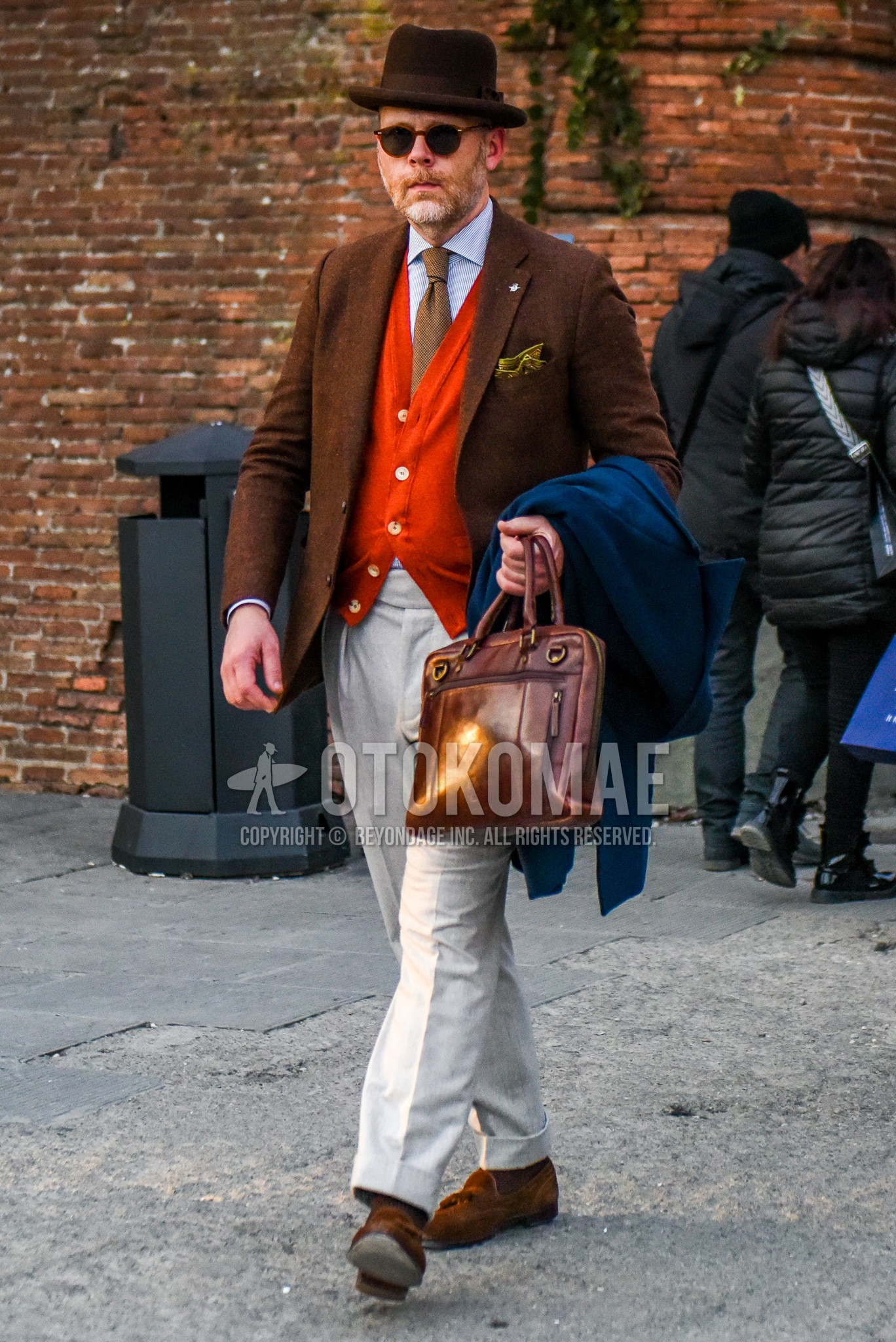 Men's winter outfit with brown plain hat, brown plain tailored jacket, light blue plain shirt, red plain cardigan, white plain slacks, brown plain briefcase/handbag.