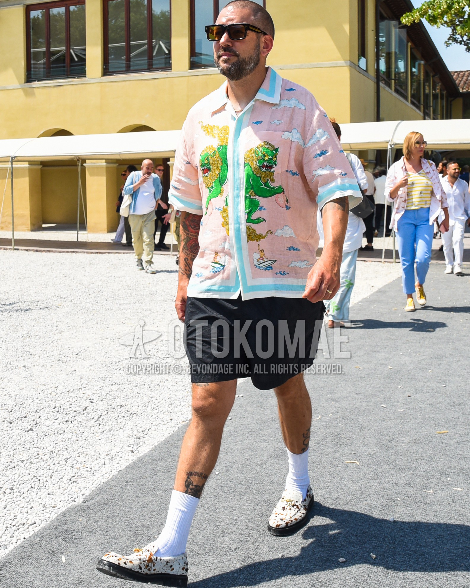 Men's spring summer outfit with brown plain sunglasses, pink graphic shirt, black plain short pants, white plain socks, white  loafers leather shoes.