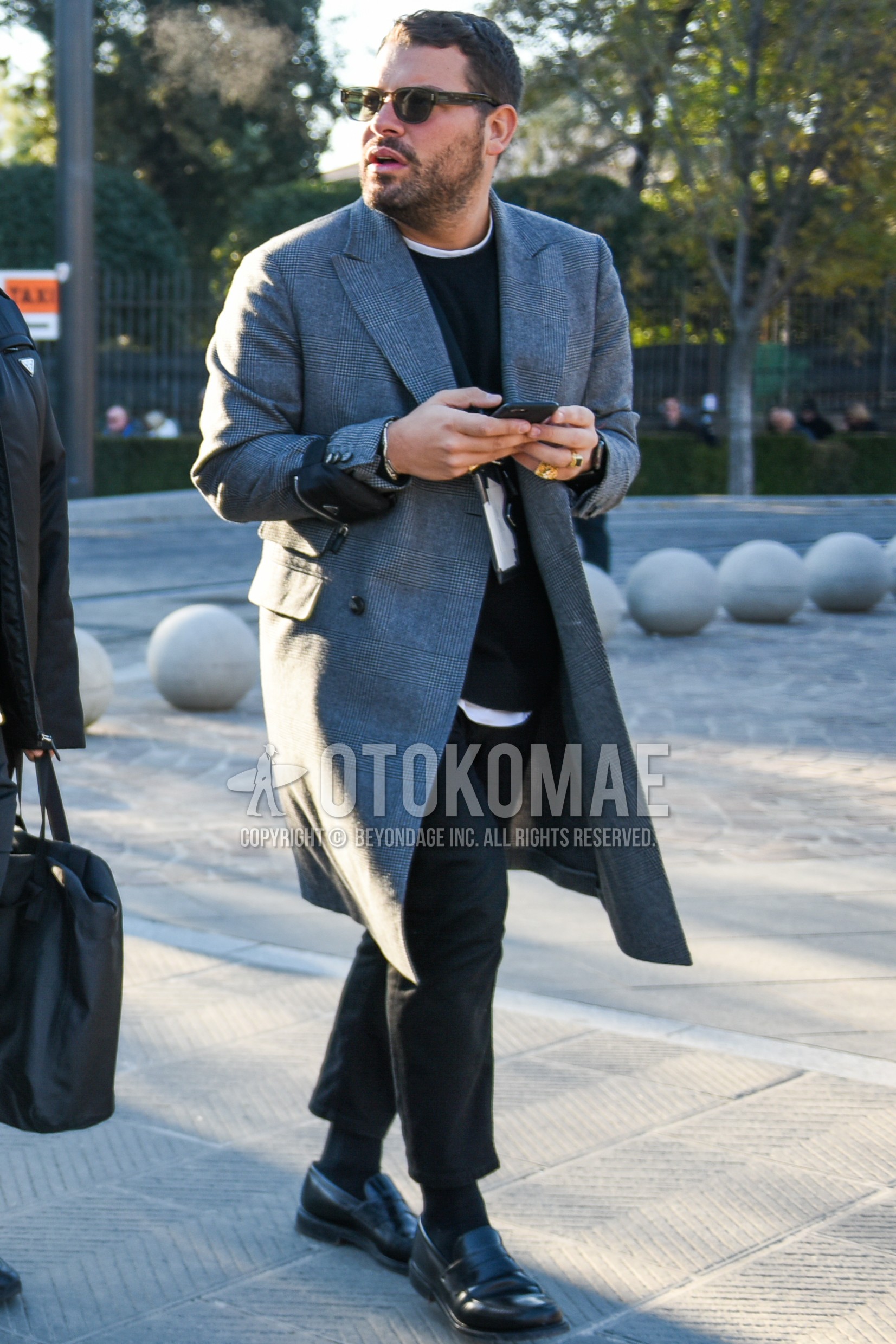 Men's autumn winter outfit with clear black plain sunglasses, gray plain chester coat, black plain sweater, gray plain cotton pants, gray plain cropped pants, dark gray plain socks, black coin loafers leather shoes.